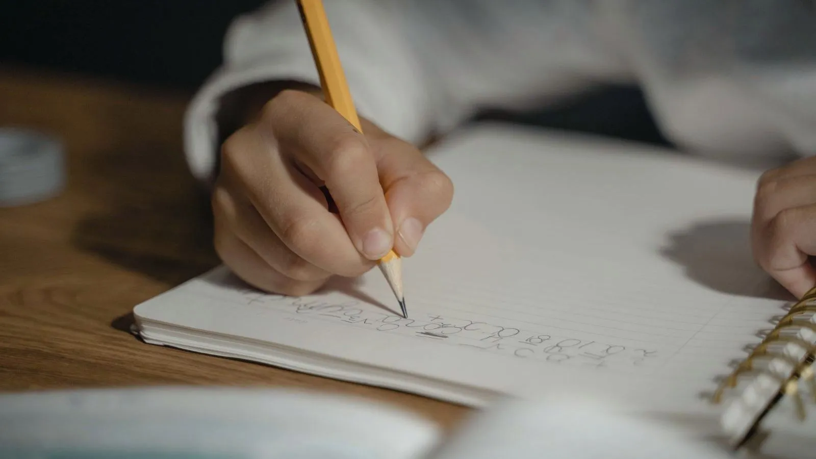 A child's hand writing in a notebook with a pencil