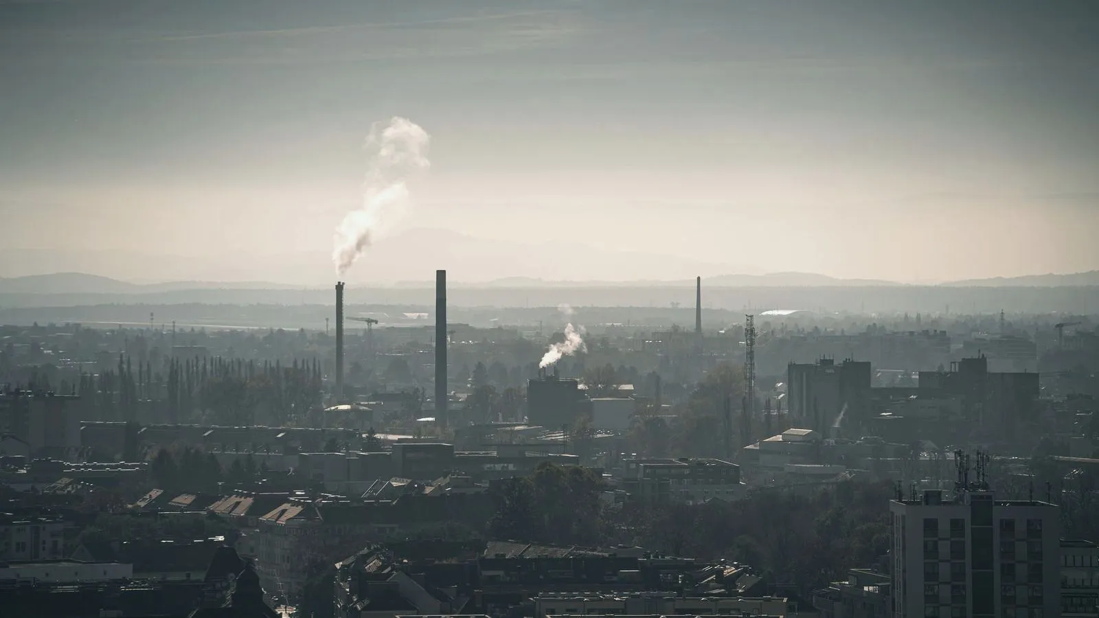 Industrial smokestacks releasing plumes over a hazy city skyline