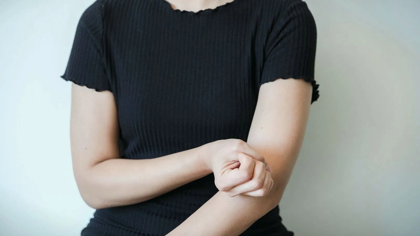 A person in a dark top scratching their forearm