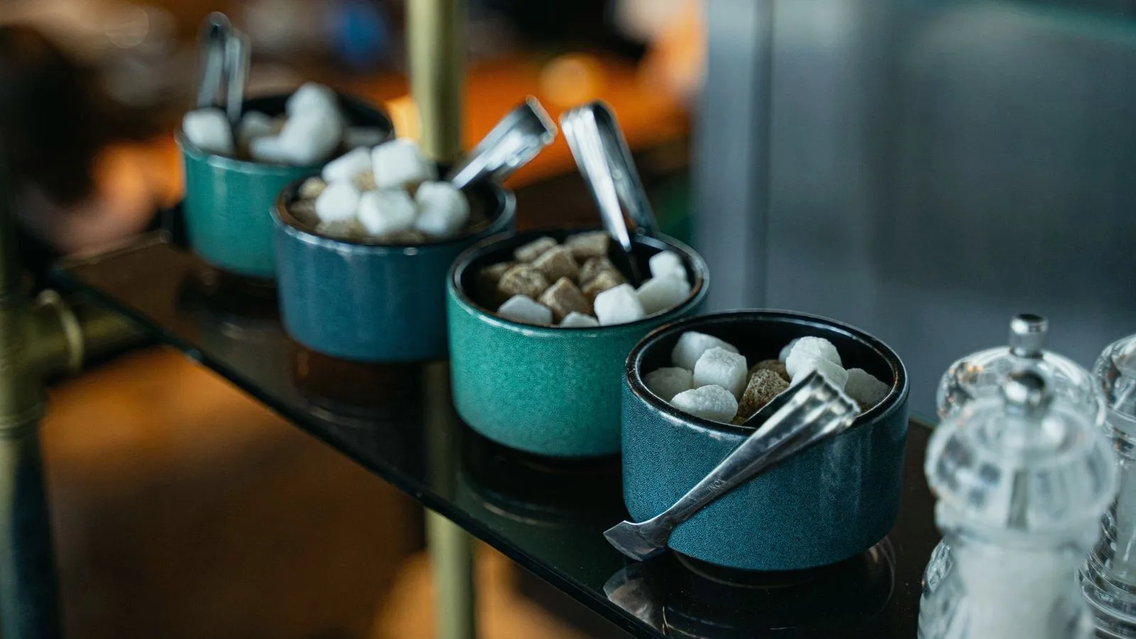 Bowls of white and brown sugar cubes with serving tongs on a cafe stand