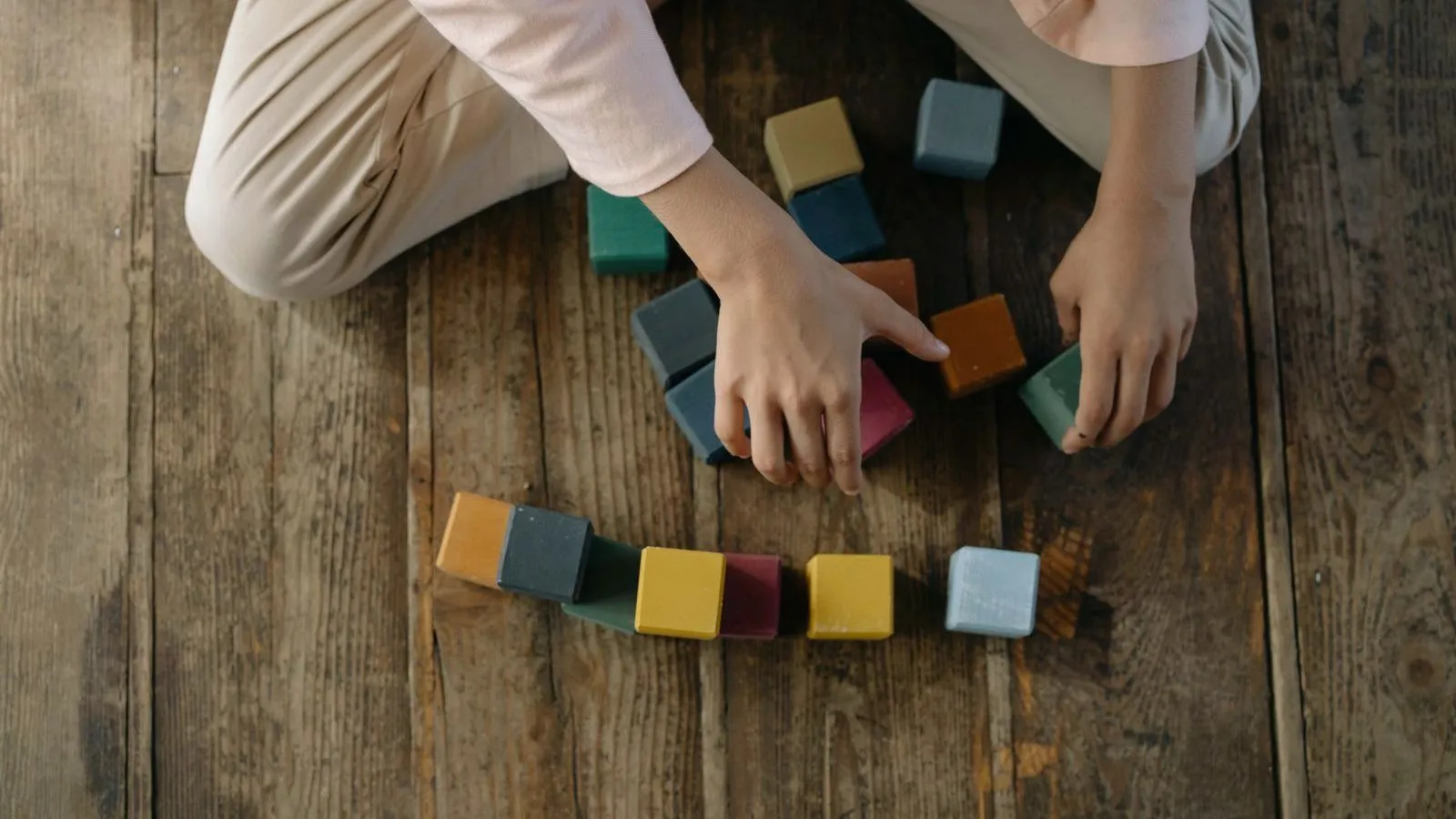 A small child's hands arranging coloured wooden blocks in a row on a wooden floor
