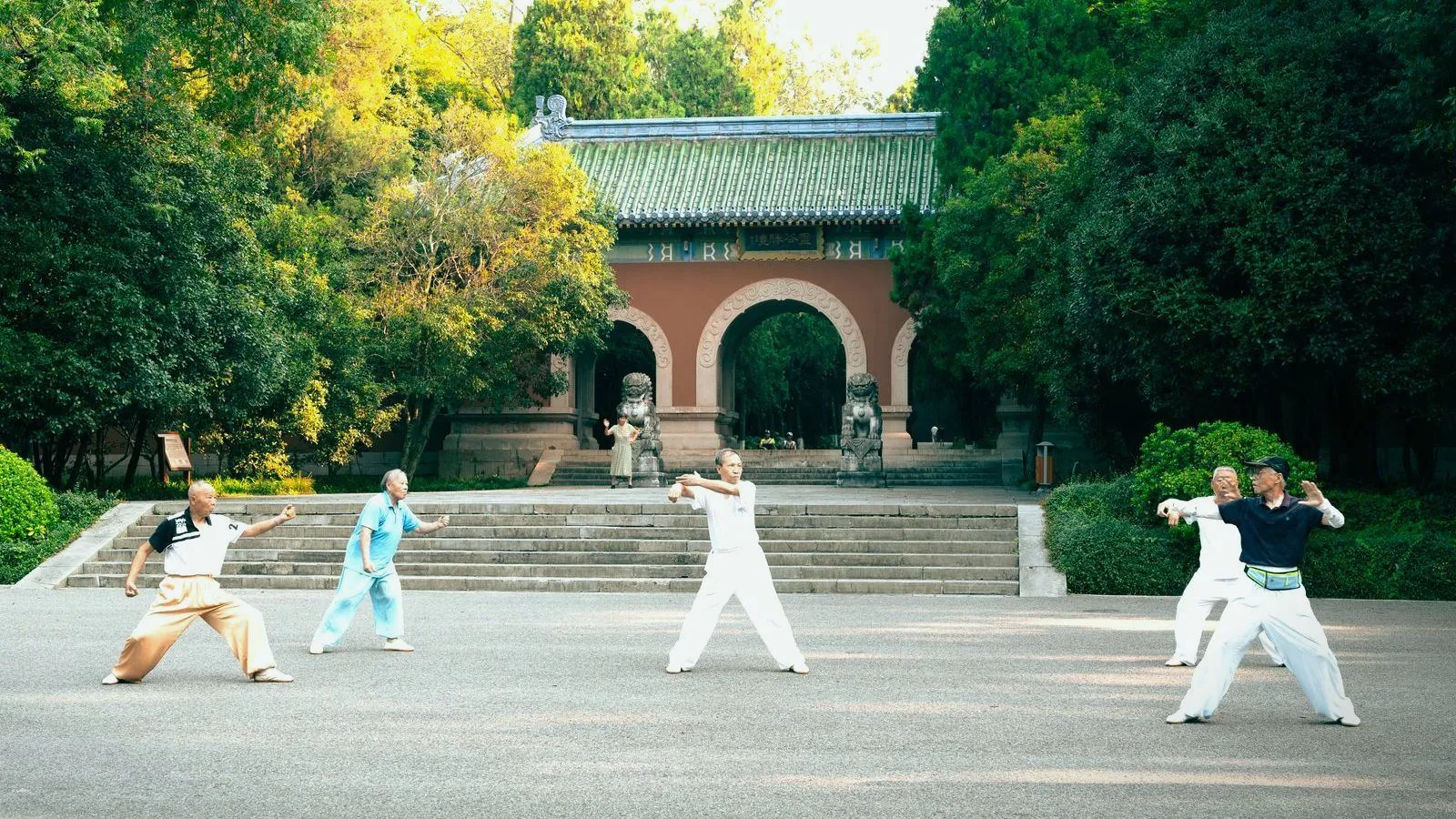 Five older people practicing a slow movement form on a paved area in a Chinese park