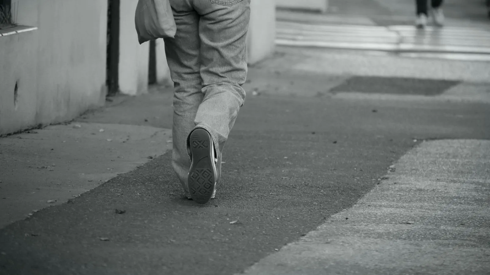 A person walking along a pavement, seen from behind at knee height