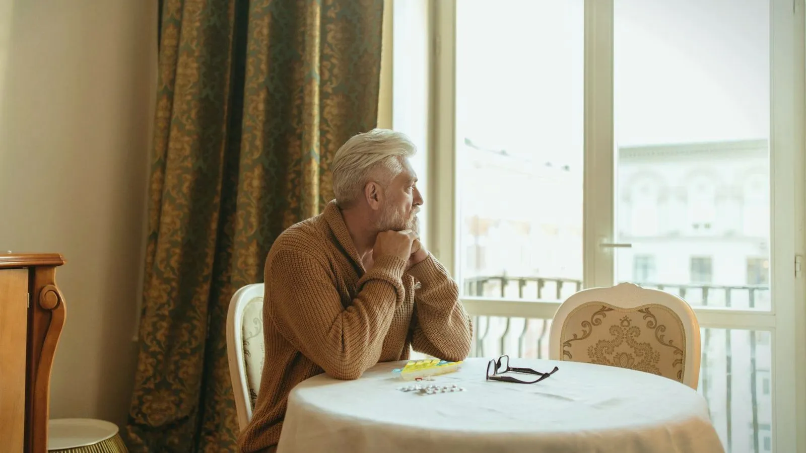 An older man sitting alone at a table by a bright window