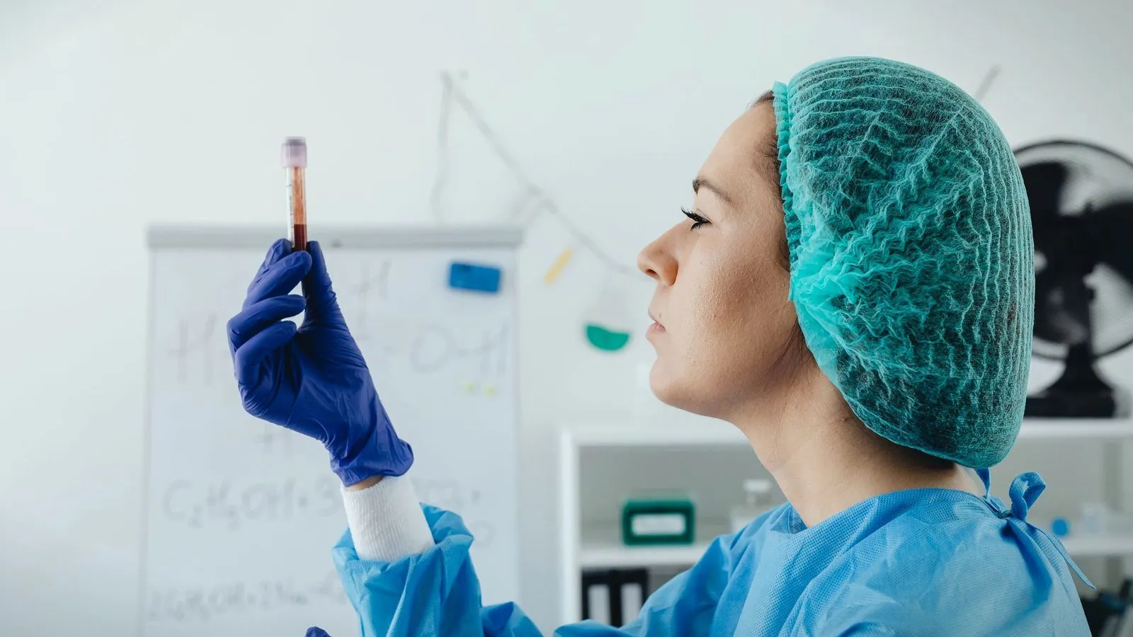 A gloved lab worker holding a blood sample tube up to the light