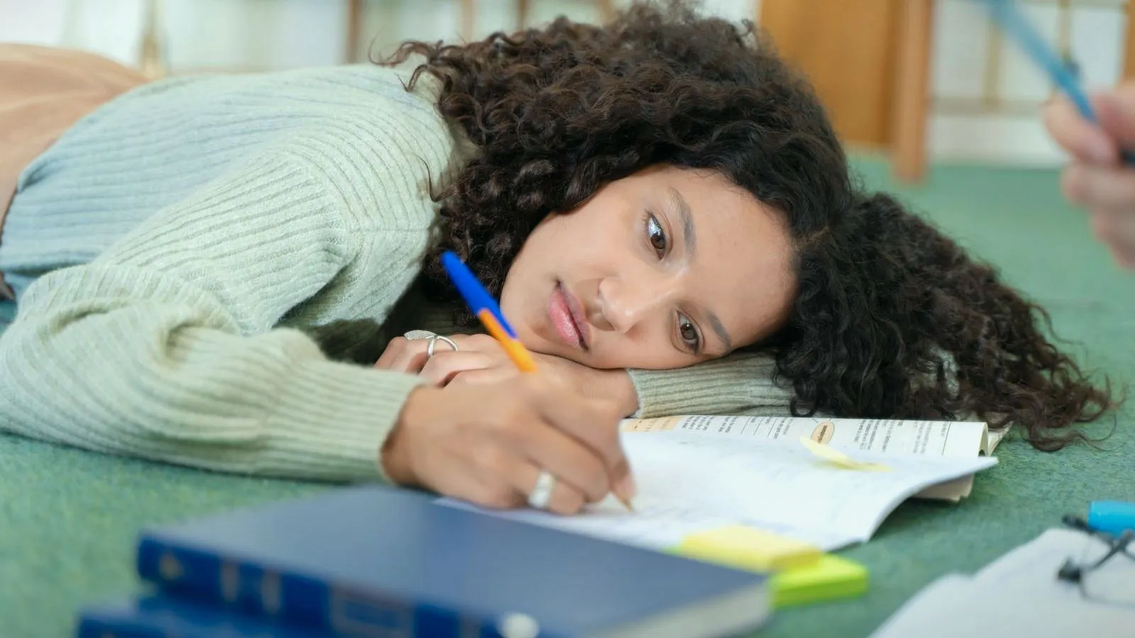 A young woman resting her head on her arm while writing in a workbook on the floor