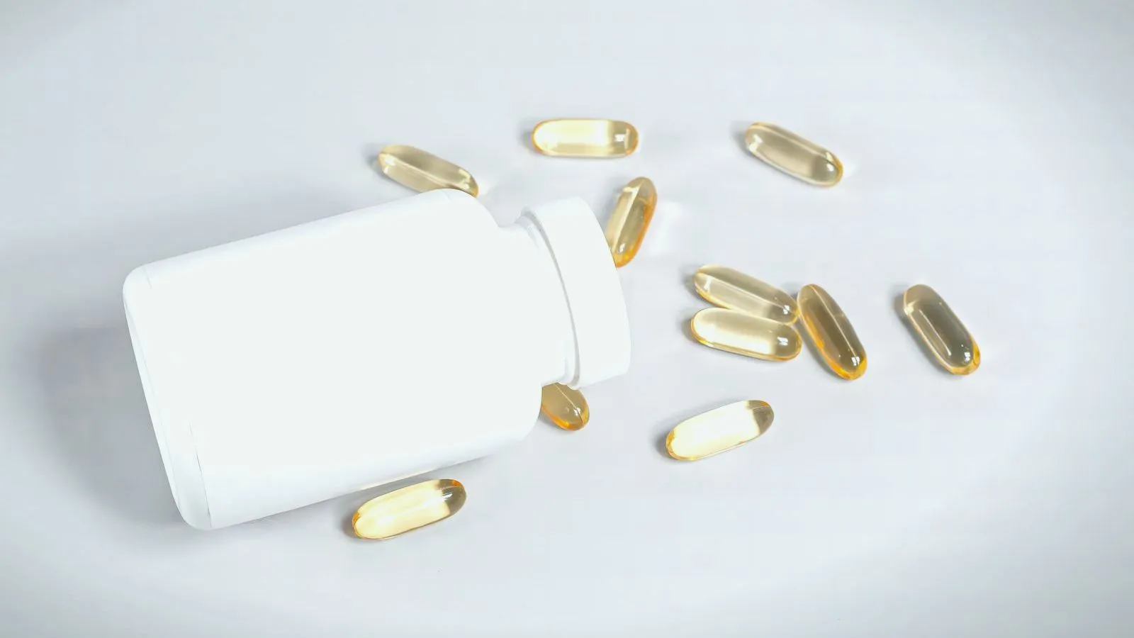 Yellow softgel supplement capsules spilling from a white bottle