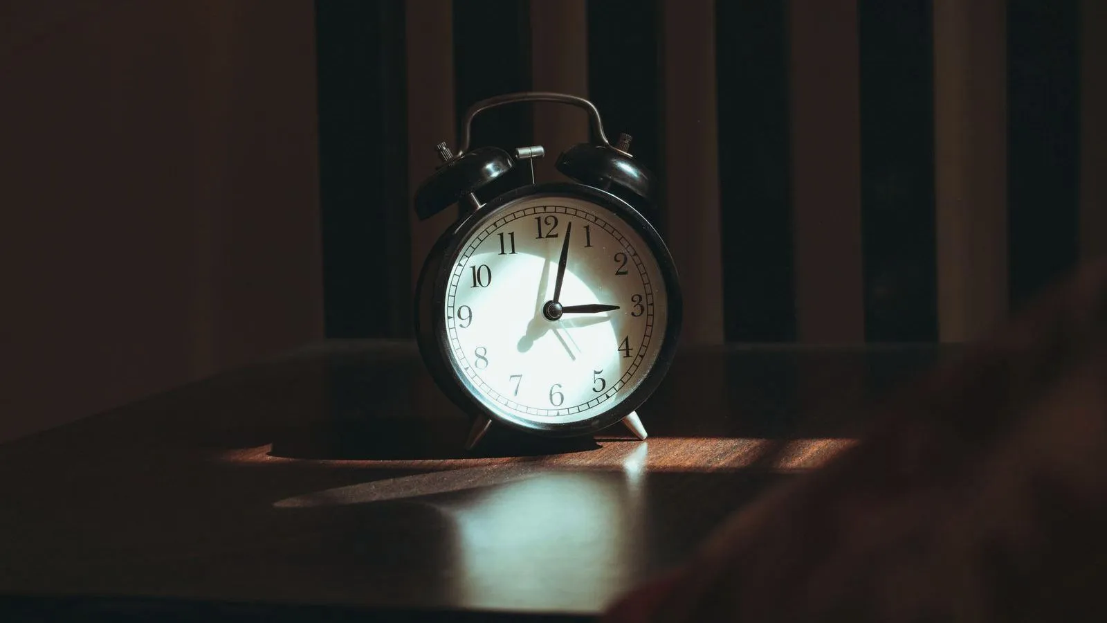A twin-bell alarm clock on a wooden surface in low, warm early light