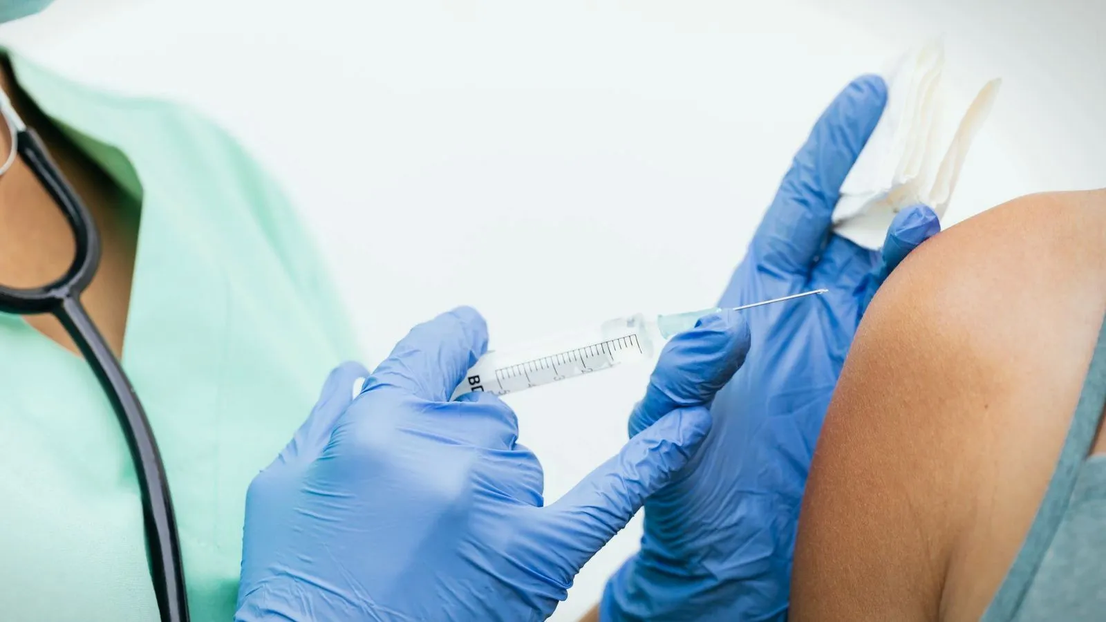 A gloved clinician giving an injection into an upper arm