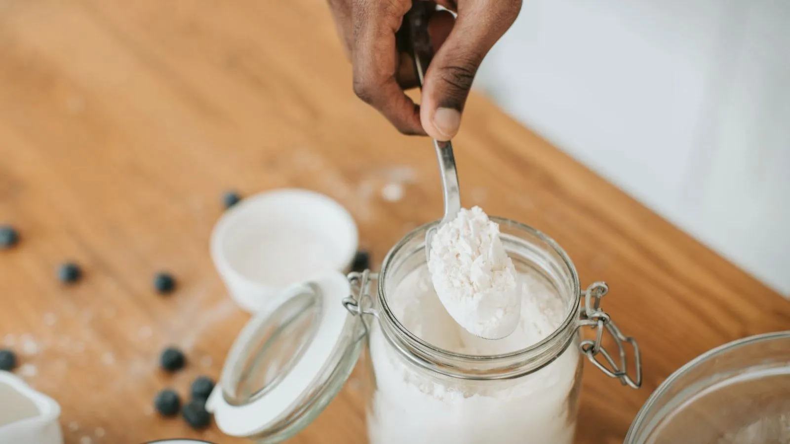A spoonful of white powder lifted from a glass storage jar on a wooden bench