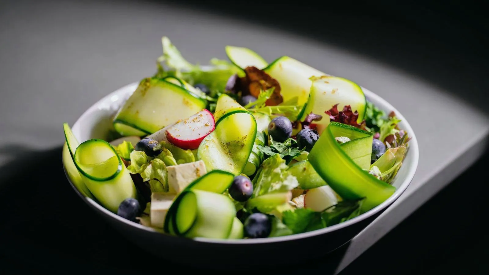 A bowl of salad with cucumber ribbons, blueberries and radish