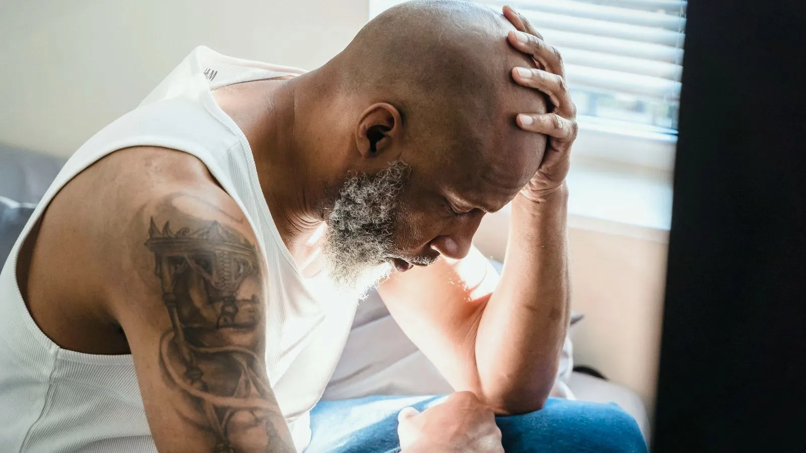 An older man sitting on a bed with his head resting in his hand