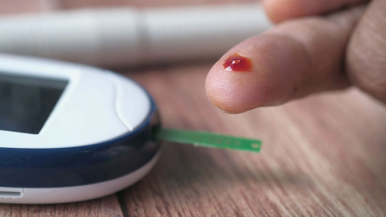 A close-up of a blood glucose meter beside a fingertip blood sample