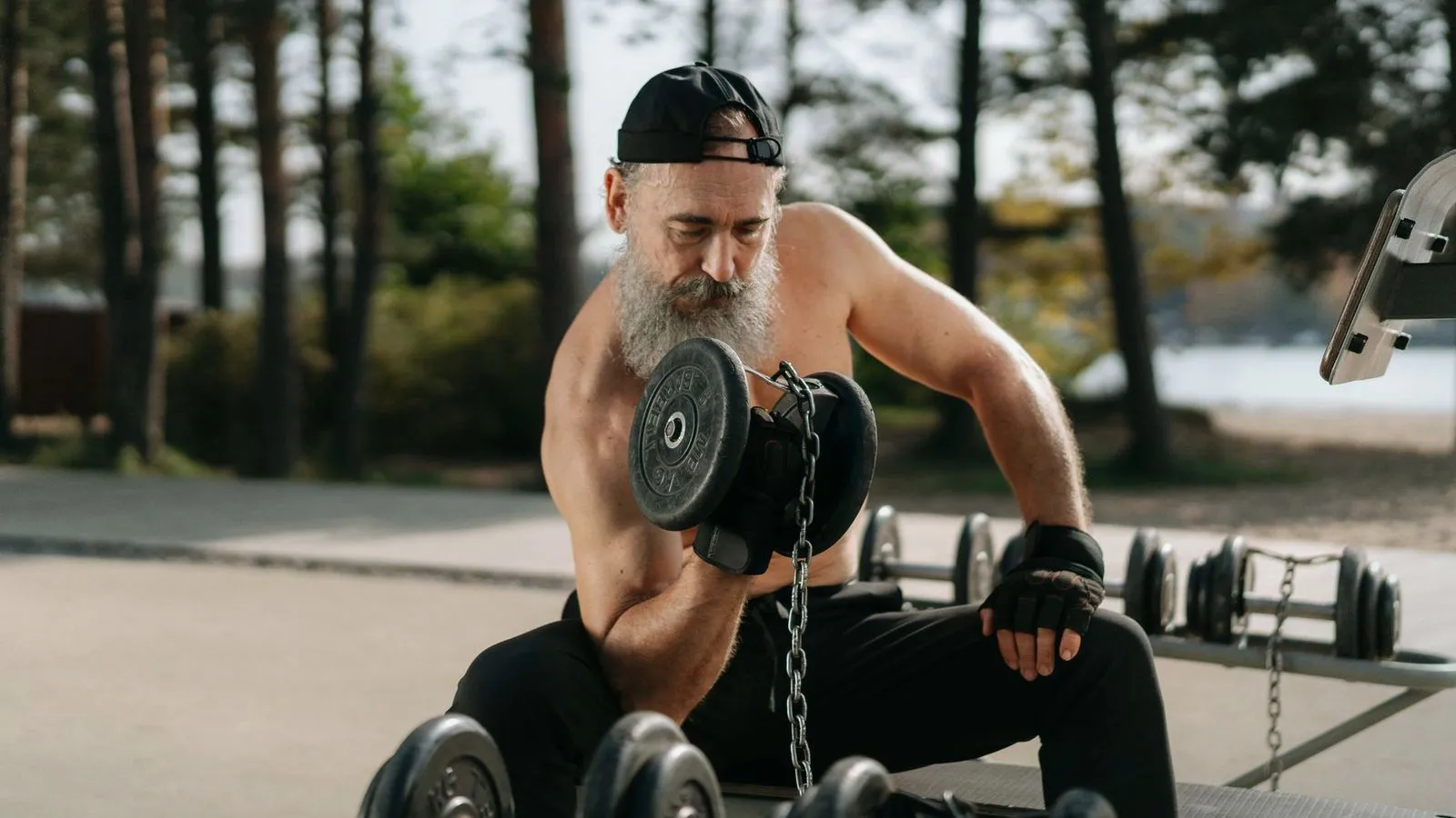 An older bearded man lifting a dumbbell at an outdoor gym