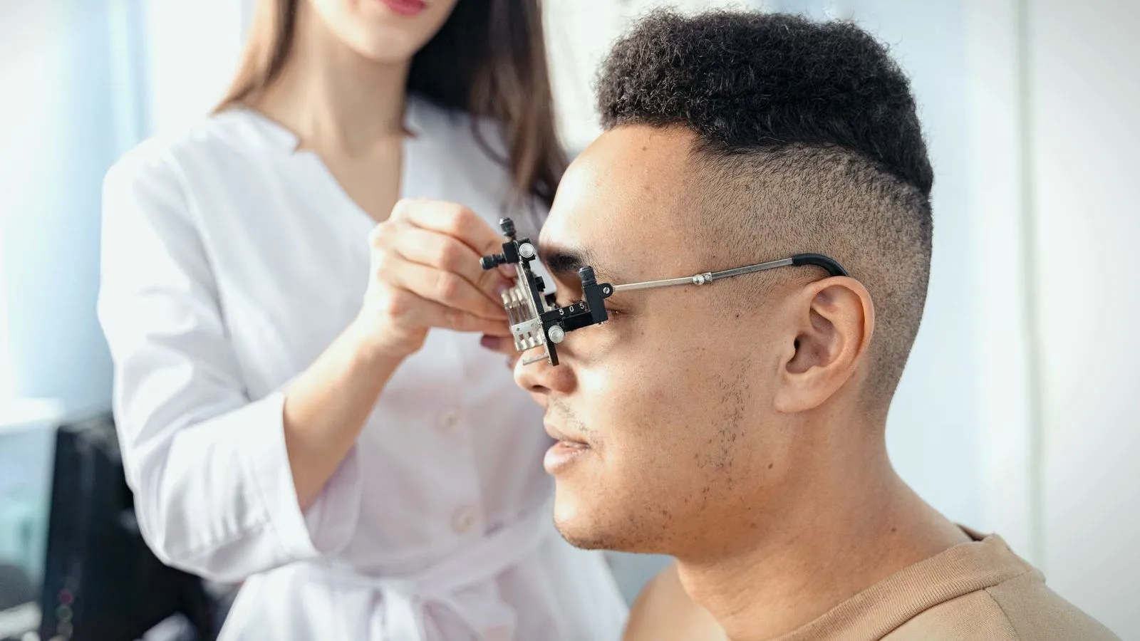 A clinician in a white coat fitting trial lenses to an adult man's eye in a clinic