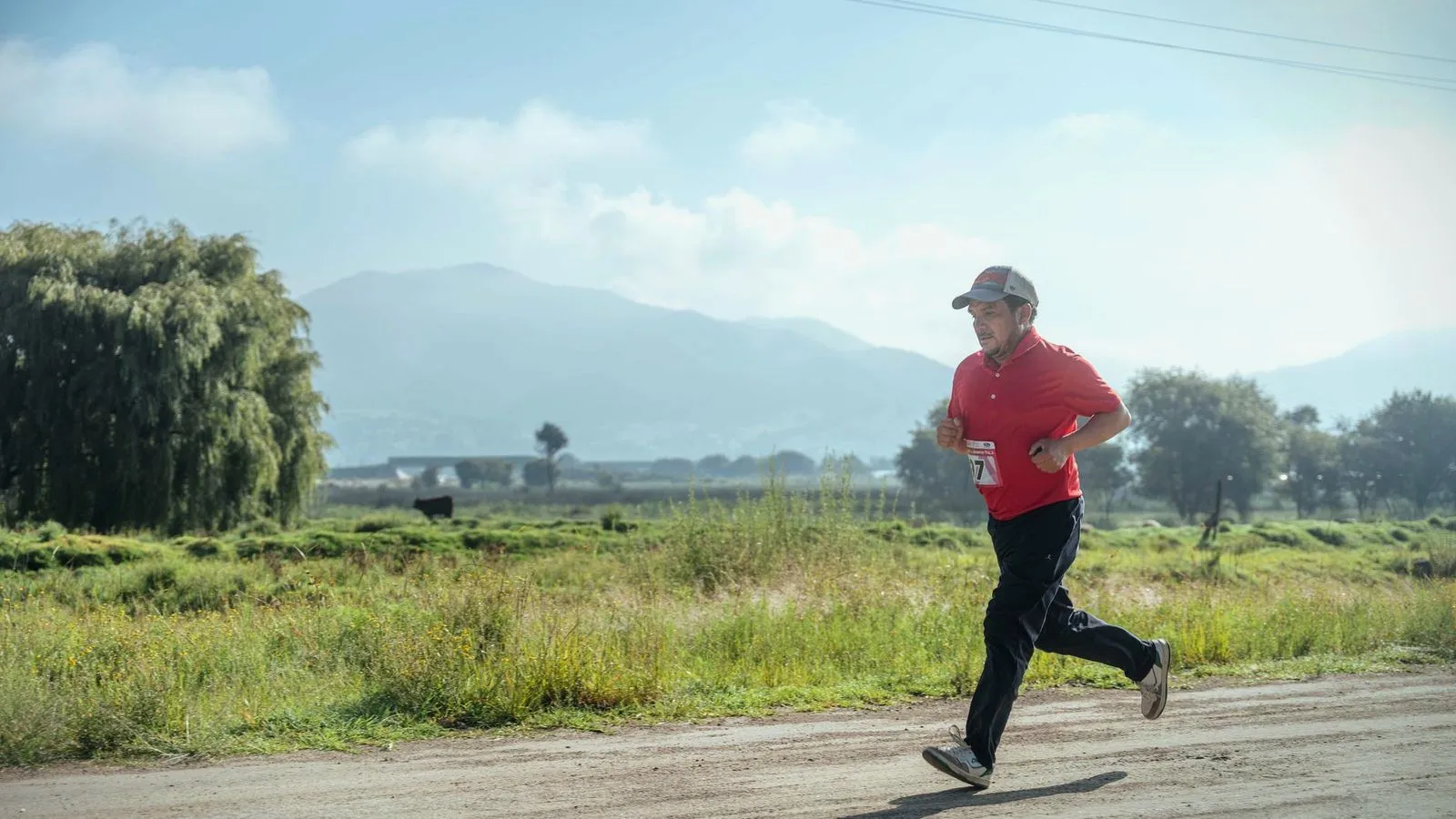An older man in a race bib running along a country road