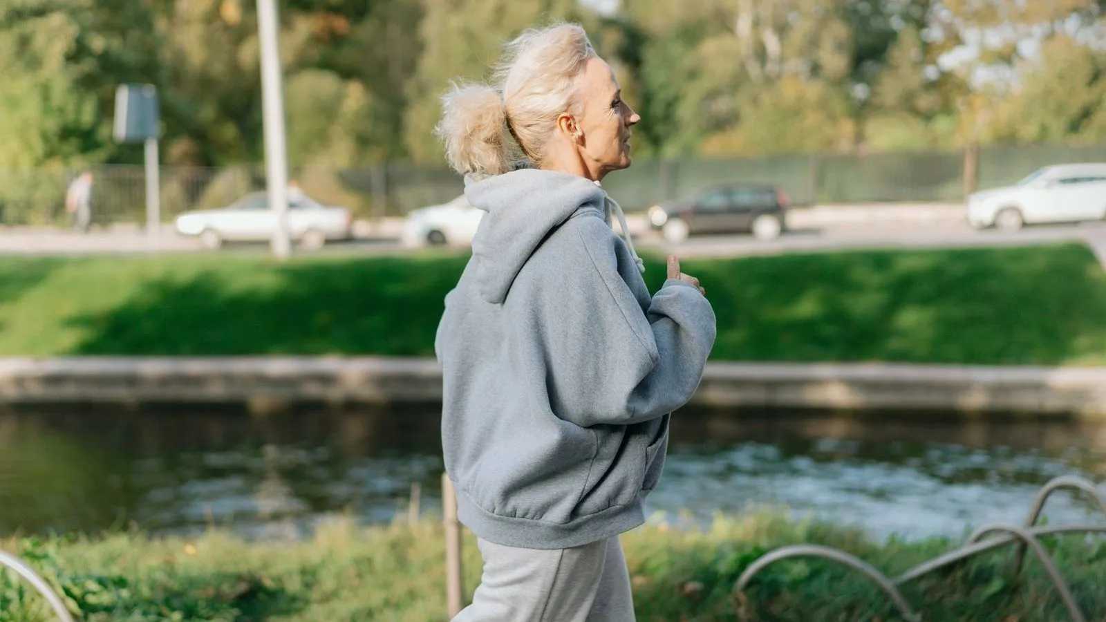 An older woman with grey hair jogging along a path beside a river