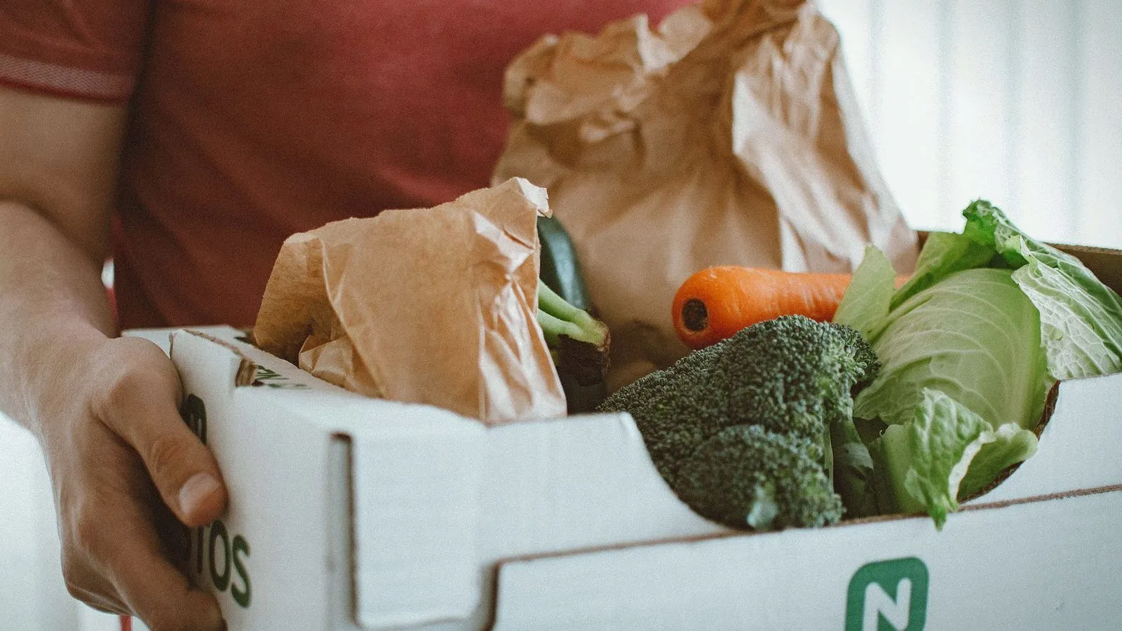 A person holding a cardboard box filled with fresh vegetables