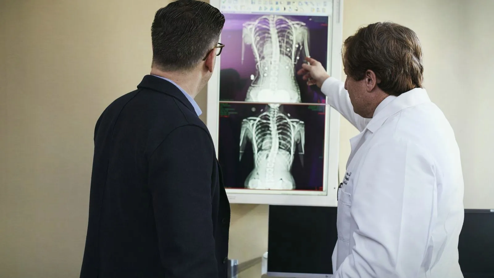 Two clinicians examining spine X-rays displayed on a lightbox