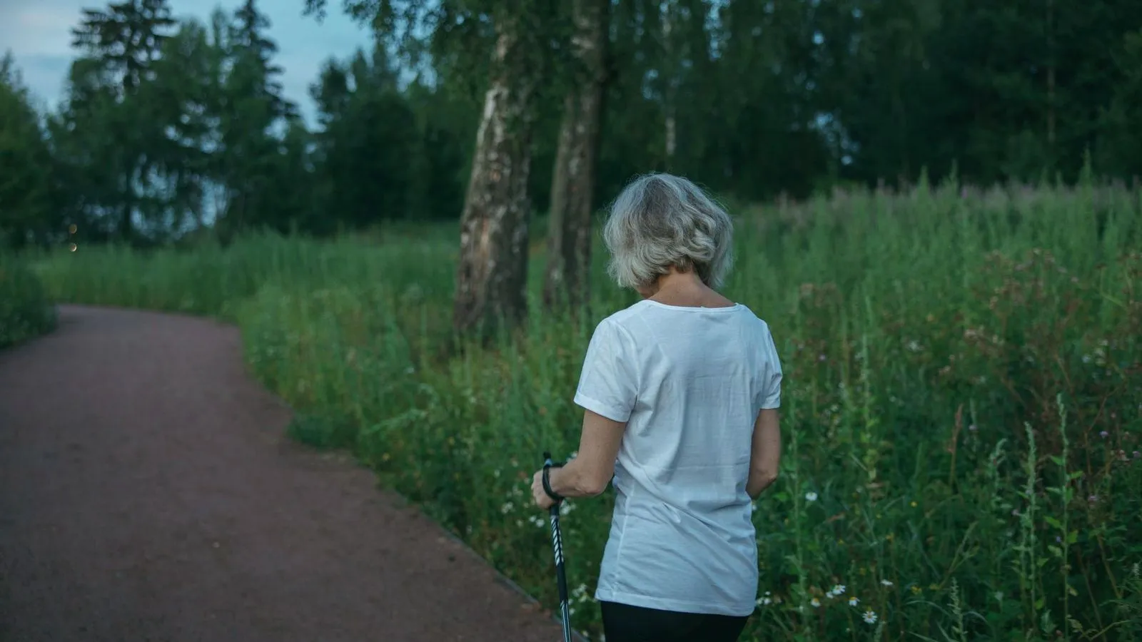 An older woman walking along a park path with a walking pole