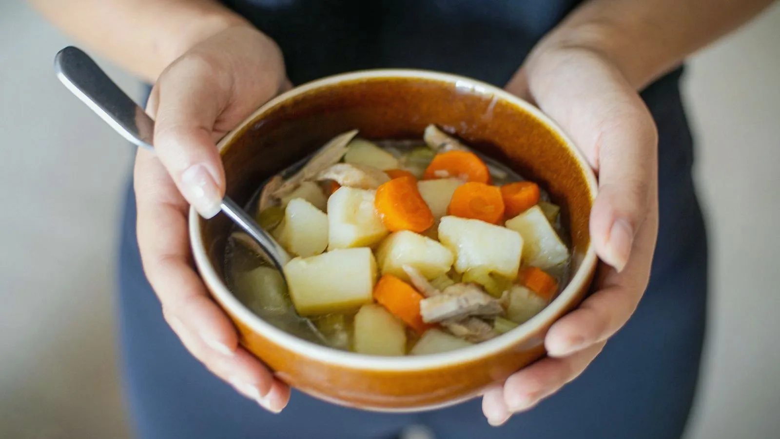 Two hands cupping a bowl of vegetable and chicken soup