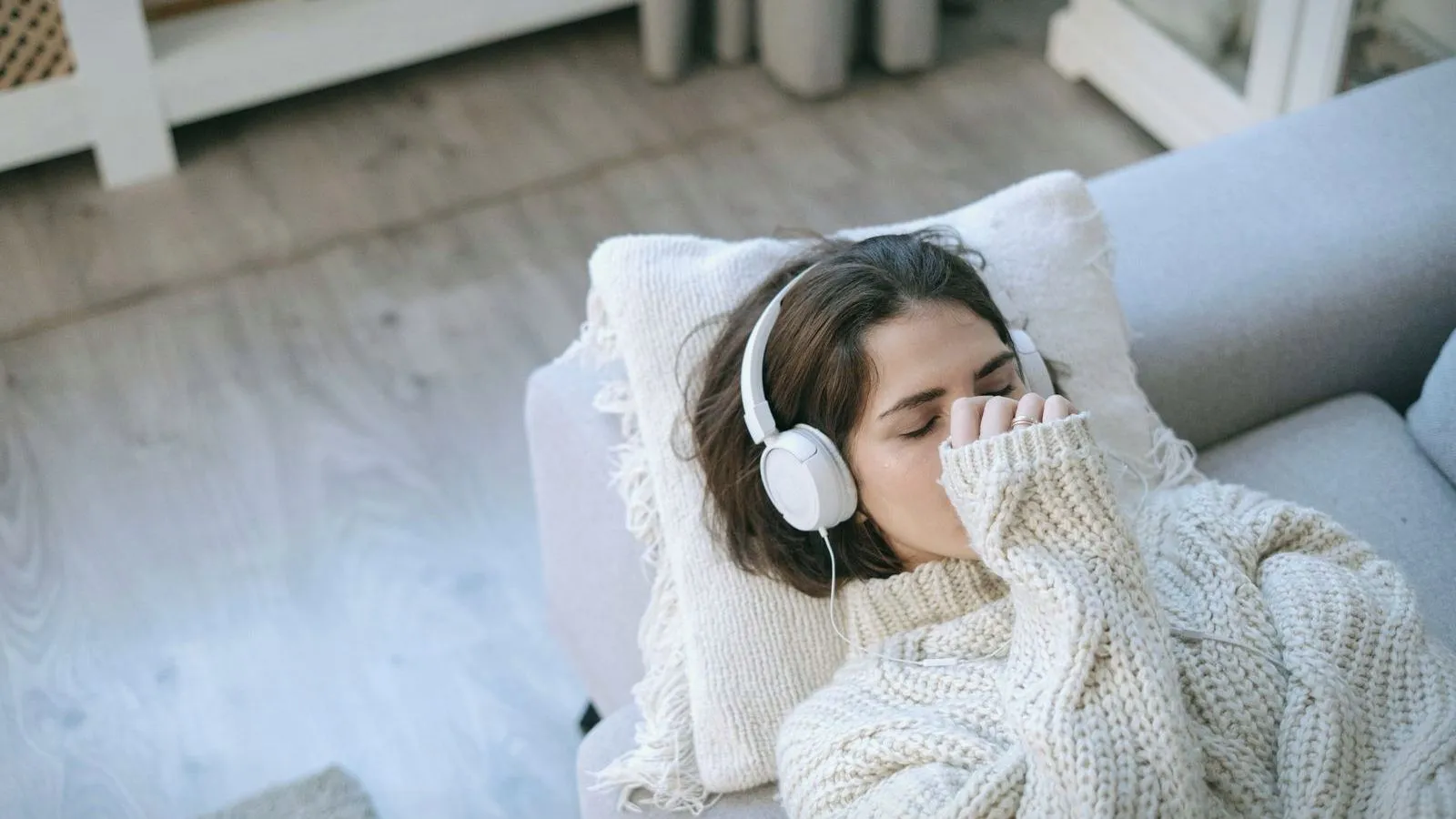 A woman resting on a sofa with headphones on and her eyes closed