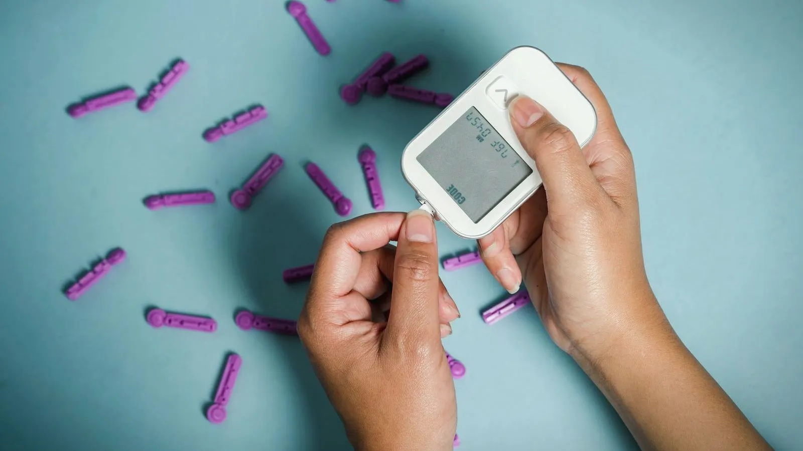 Hands using a glucose meter surrounded by test strips