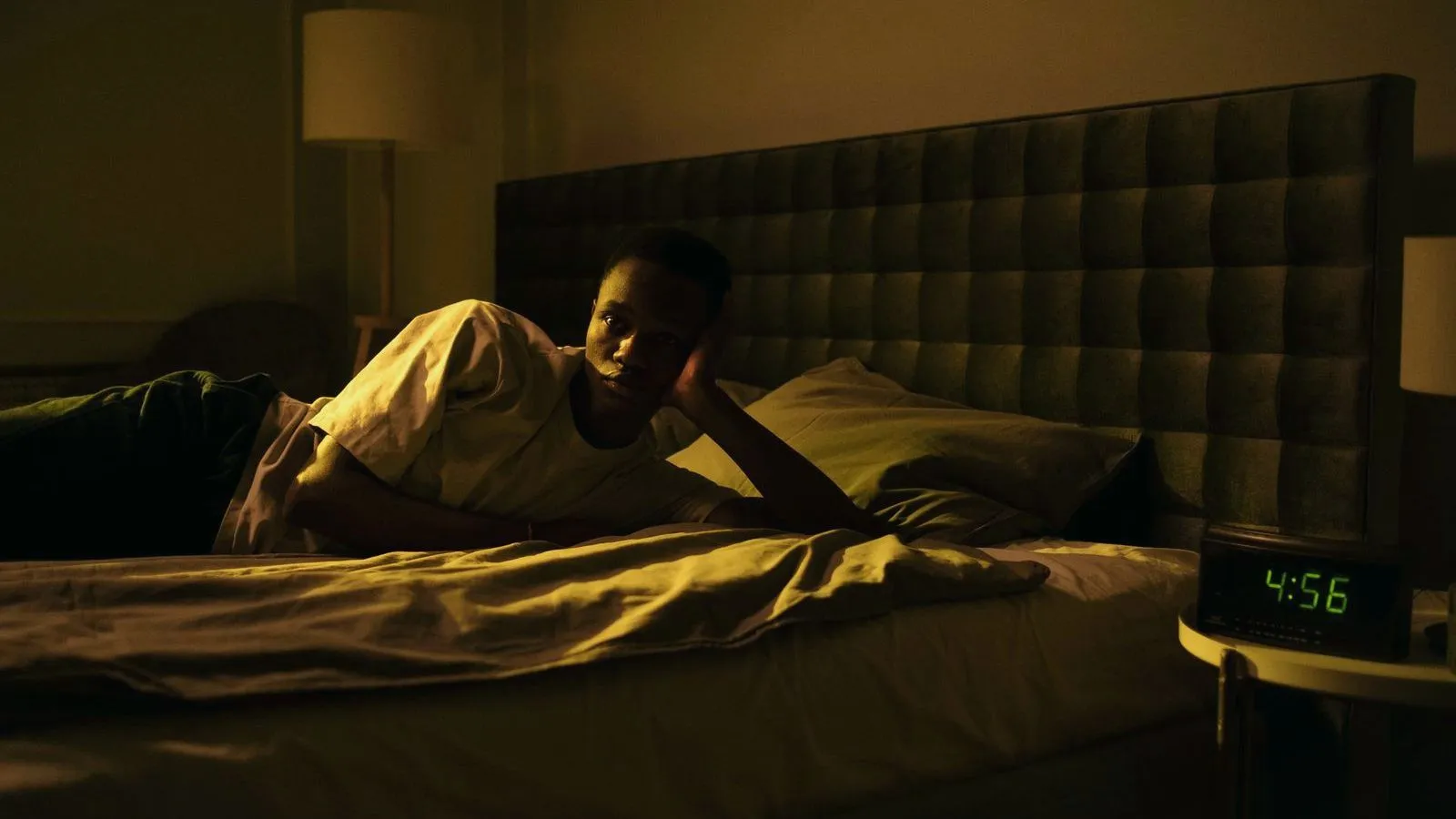 A person lying awake in a dark bedroom beside a clock reading 4:56