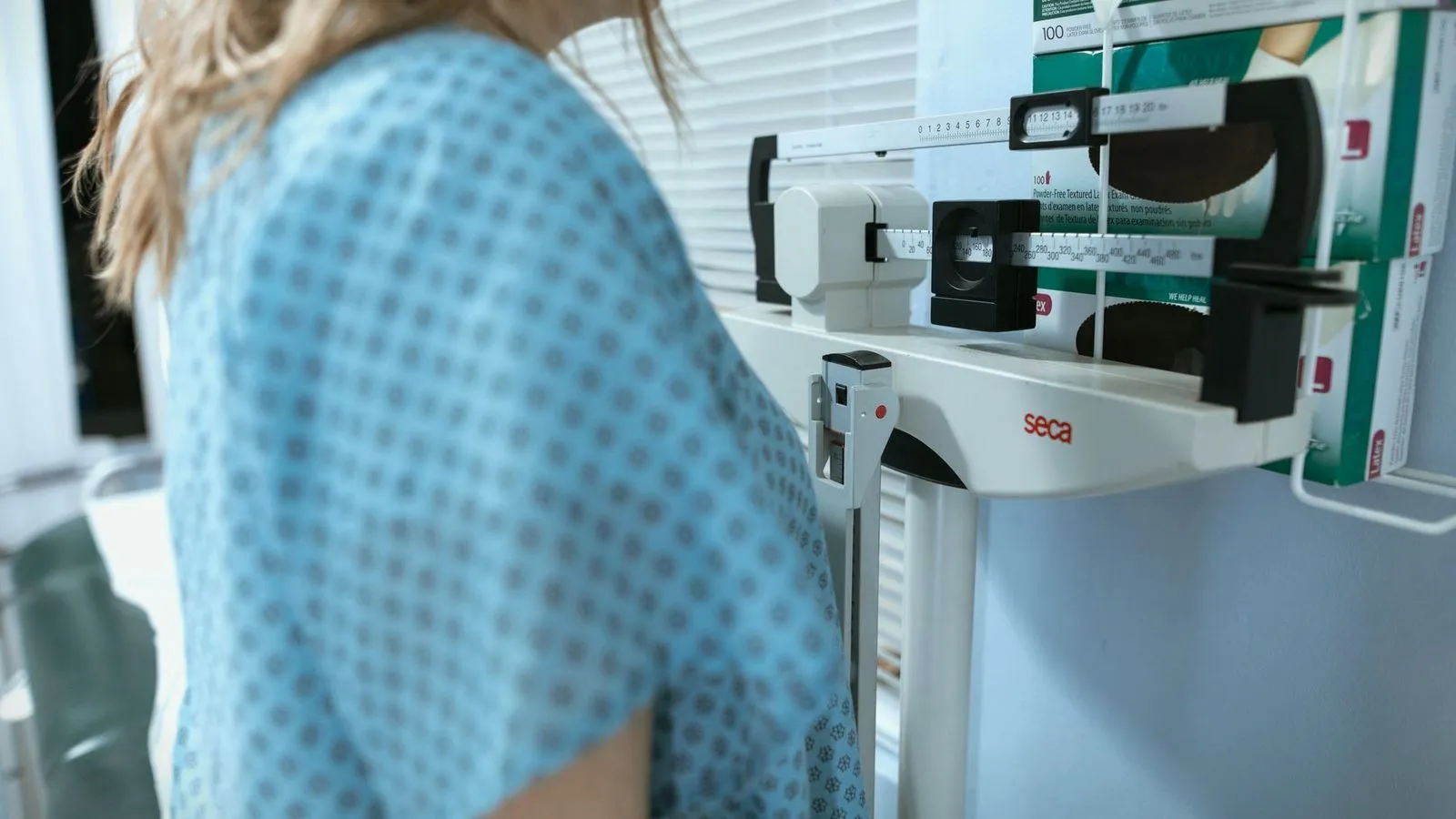 A patient in a hospital gown standing at a clinic weighing scale