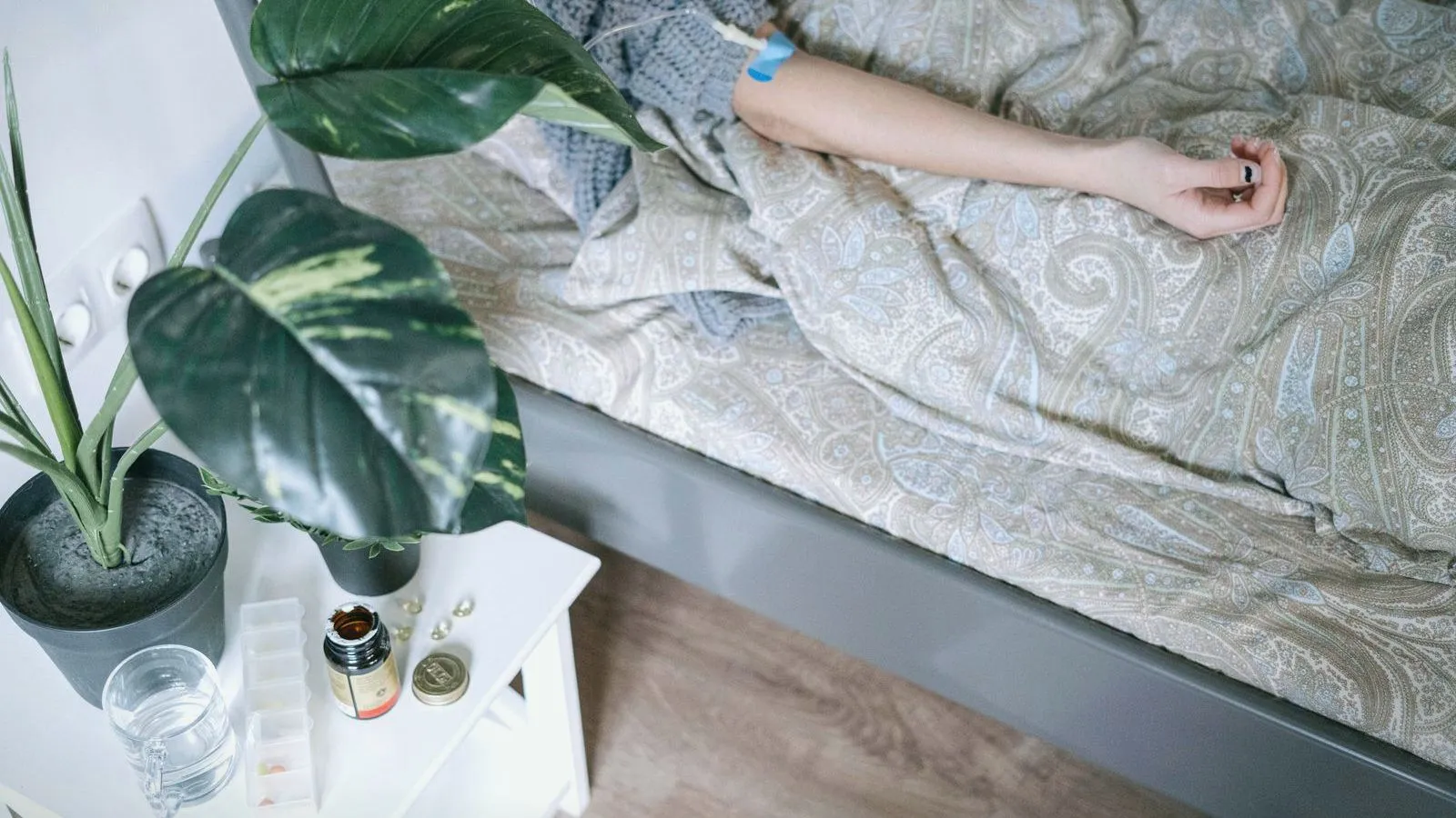 A bedside table holding a glass of water and small bottles beside an unmade bed