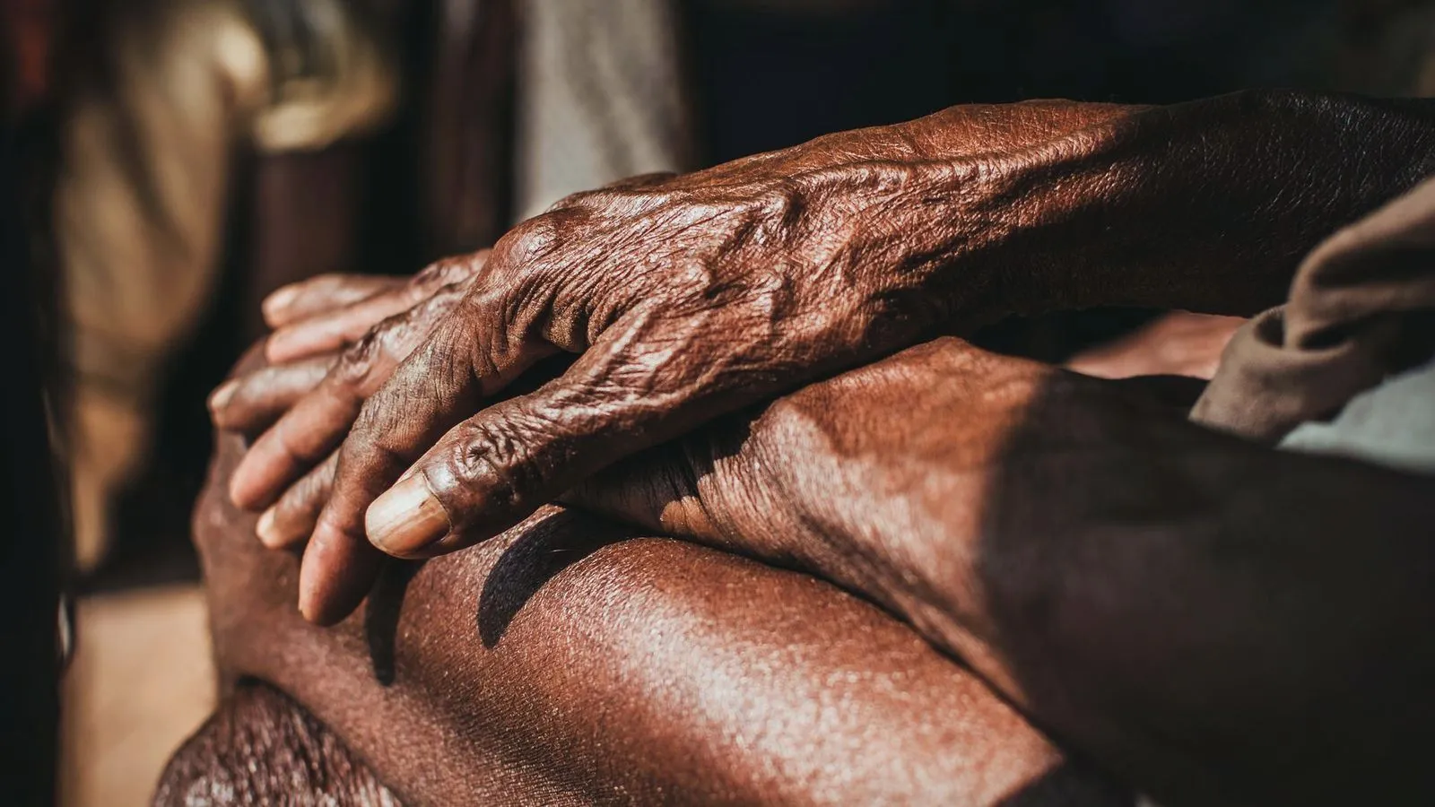 The weathered hands of an older person resting on a knee