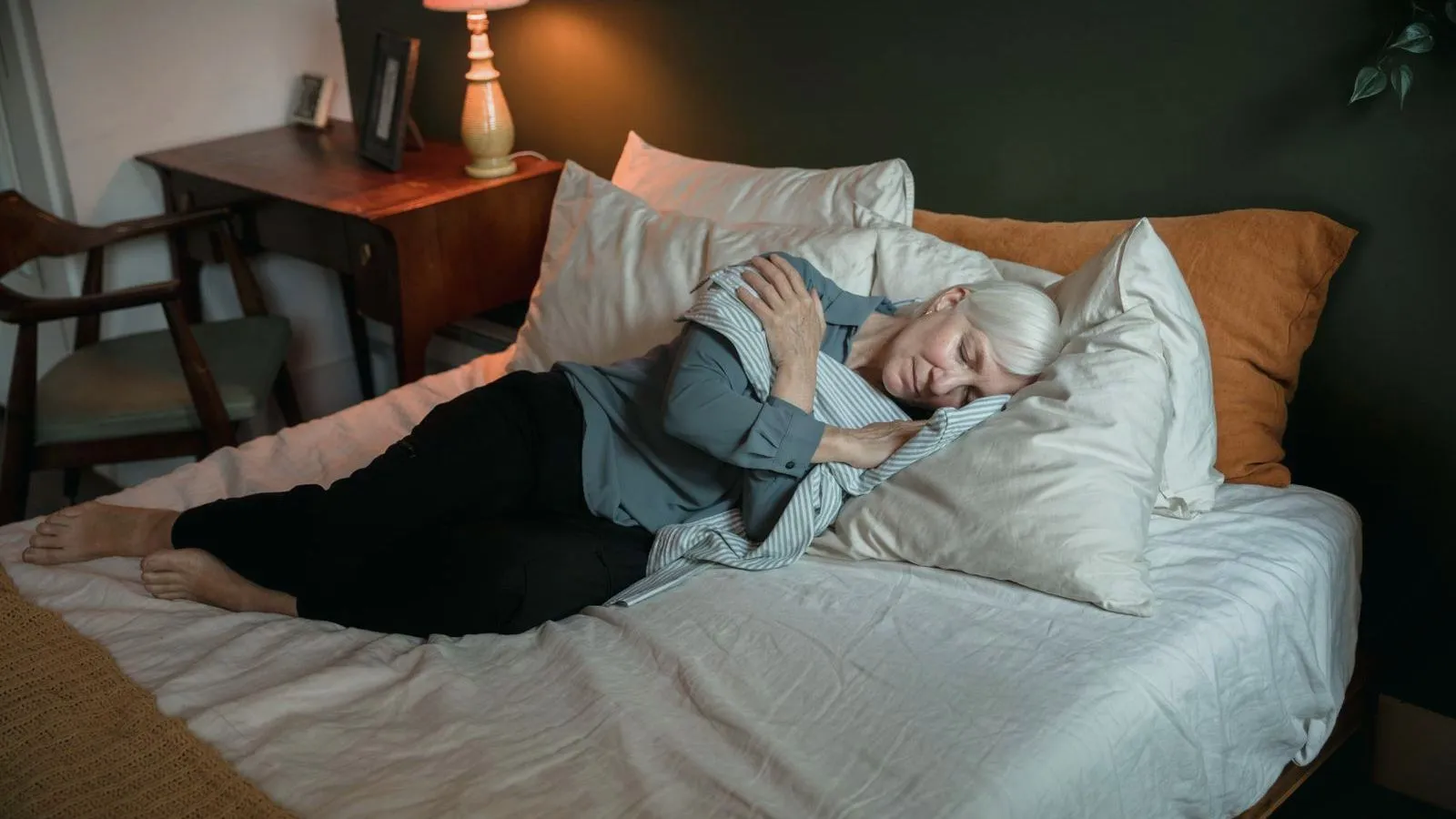 An older woman lying awake on a bed with the lamp still on