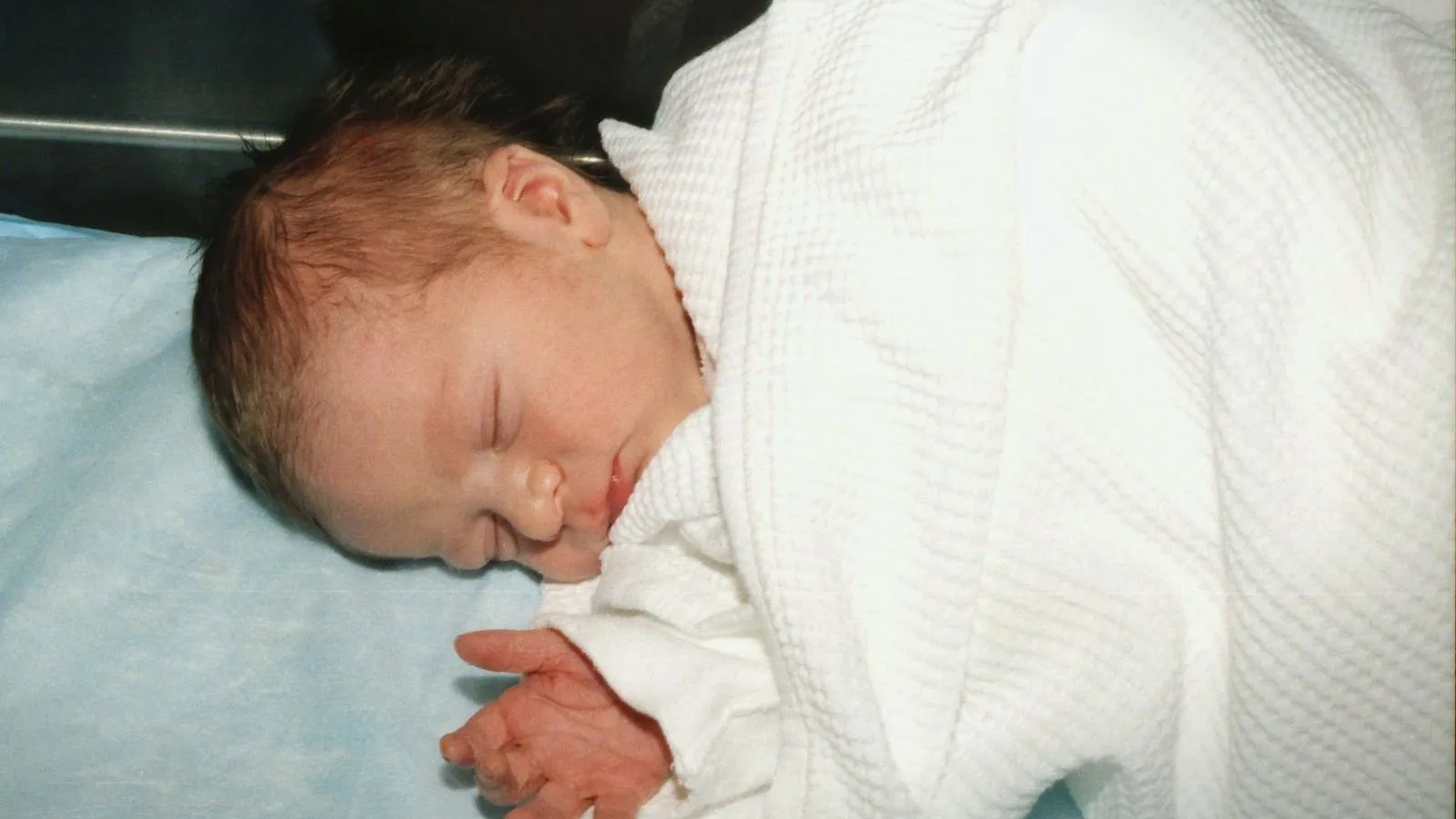 A sleeping newborn wrapped in a white hospital blanket