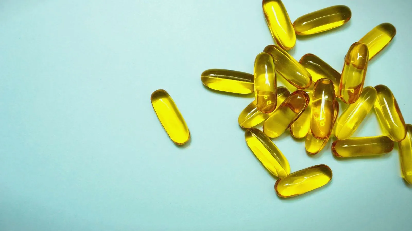 Golden fish oil capsules scattered on a pale blue background