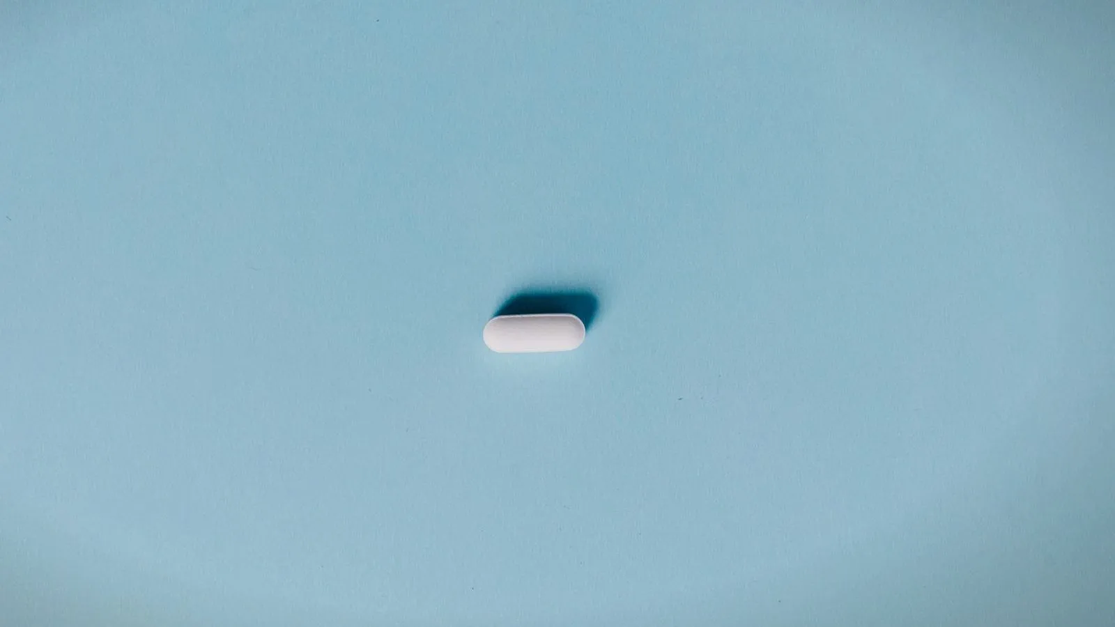 A single white oval tablet on a pale blue background