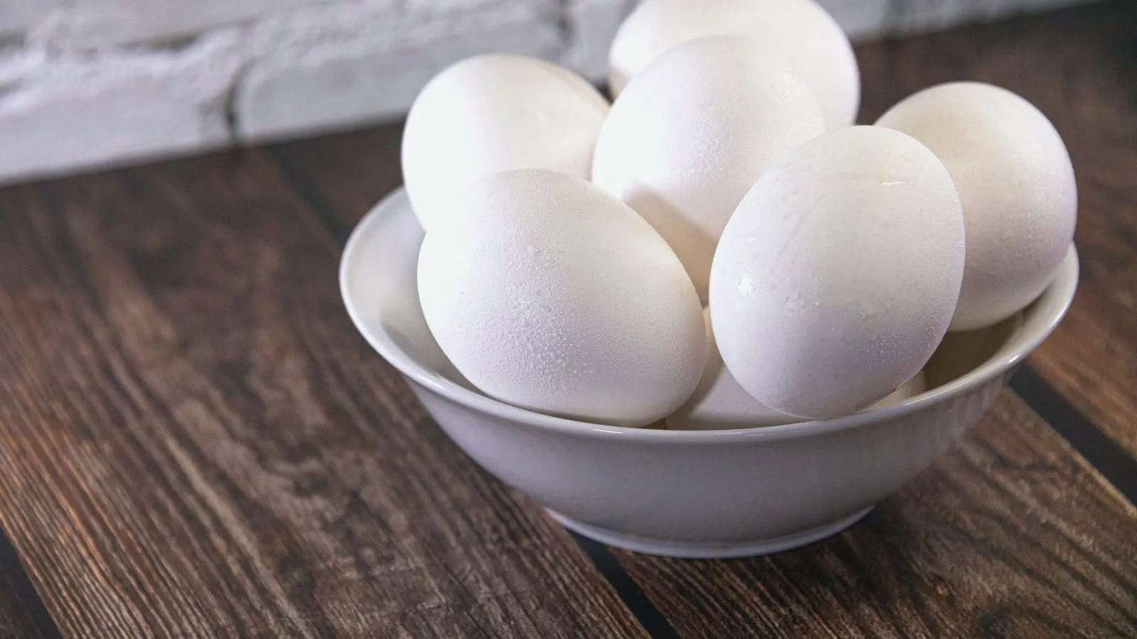 A white bowl of fresh eggs on a wooden table