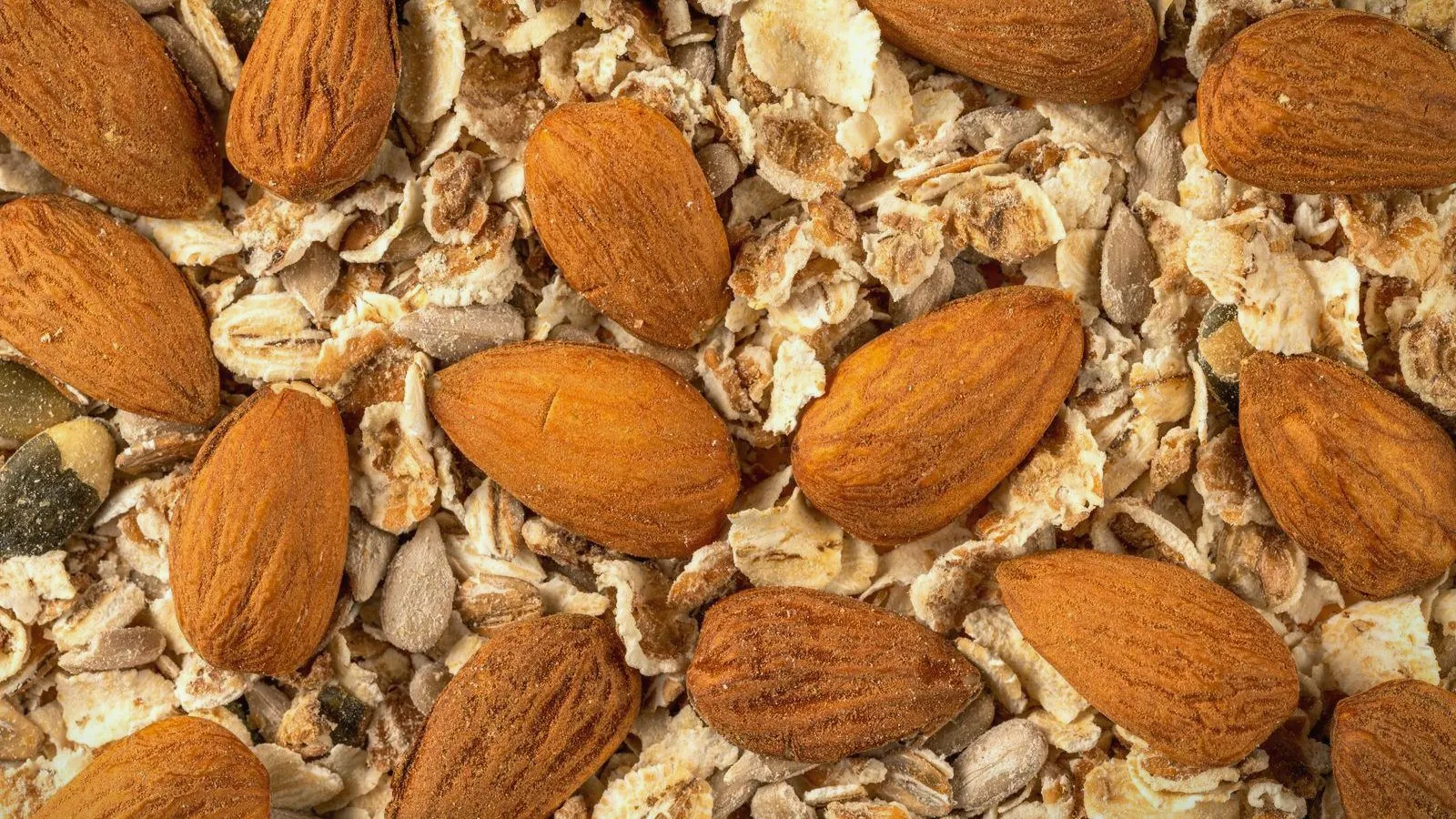 A close-up of whole almonds mixed through rolled oats, seeds and grains