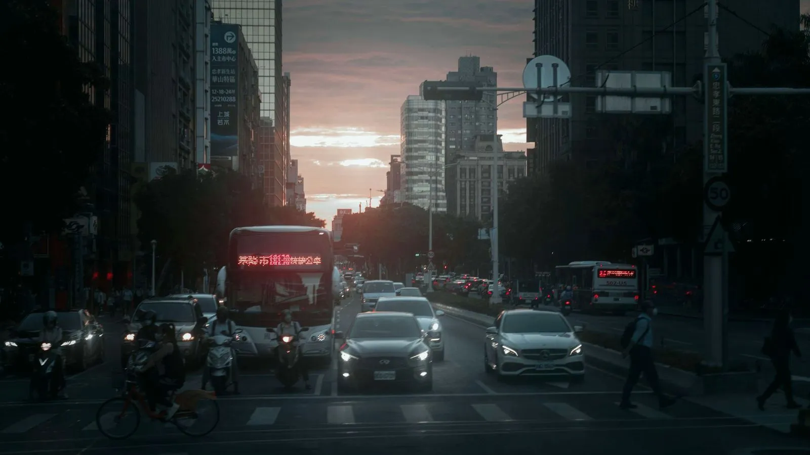 A busy city street filled with cars, buses and pedestrians at dusk