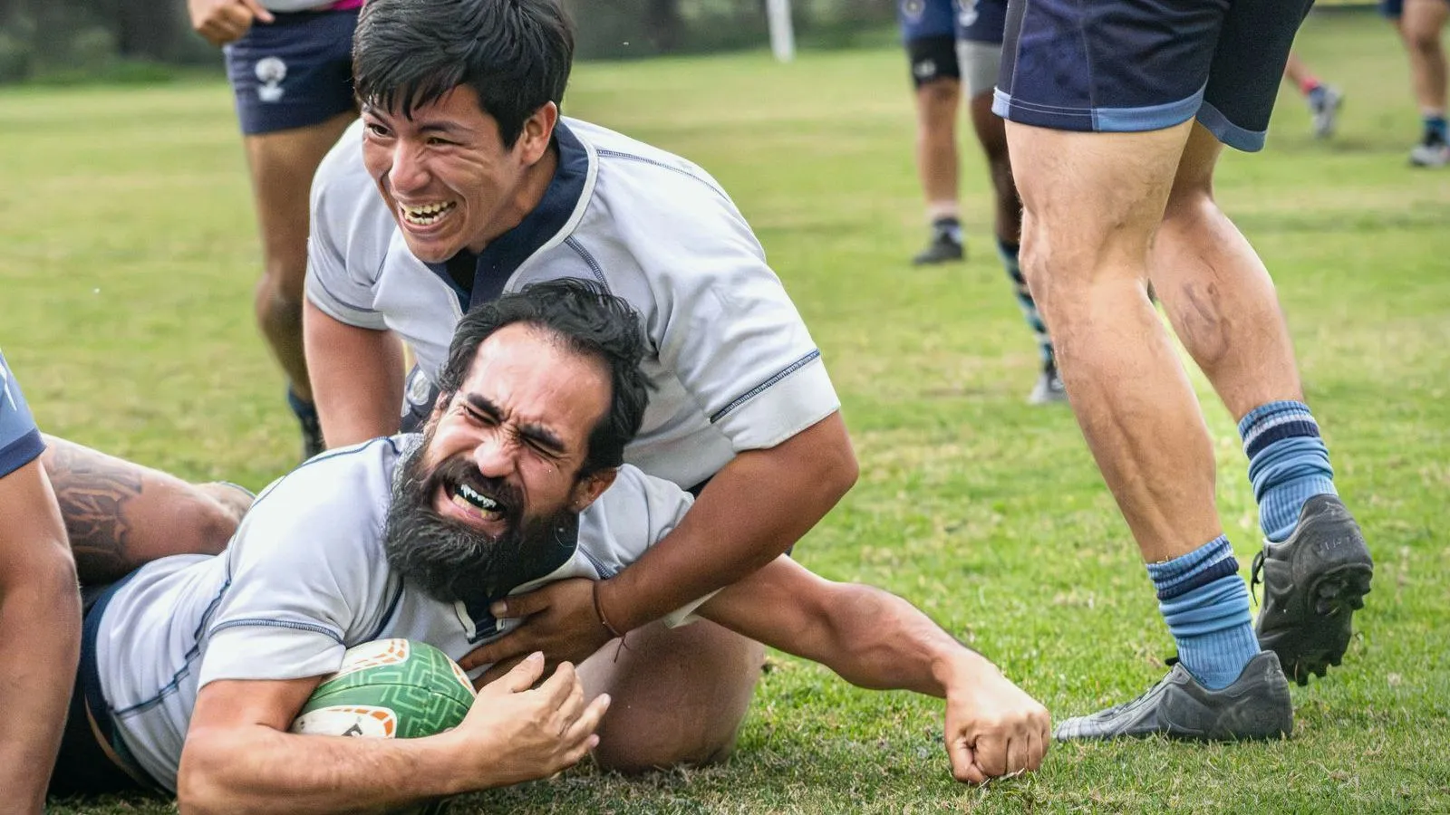 Two rugby players in matching training kit grappling on the ground over the ball