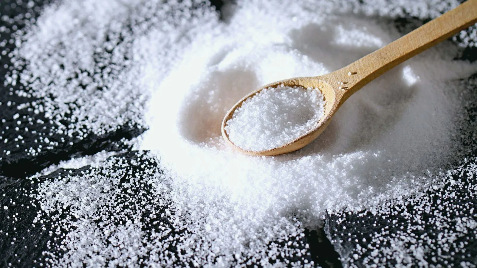 A wooden spoon of coarse salt resting on a scattering of salt crystals