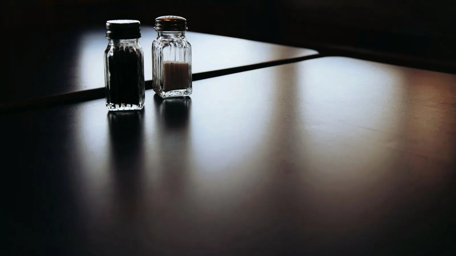 Salt and pepper shakers casting long shadows across a dark table