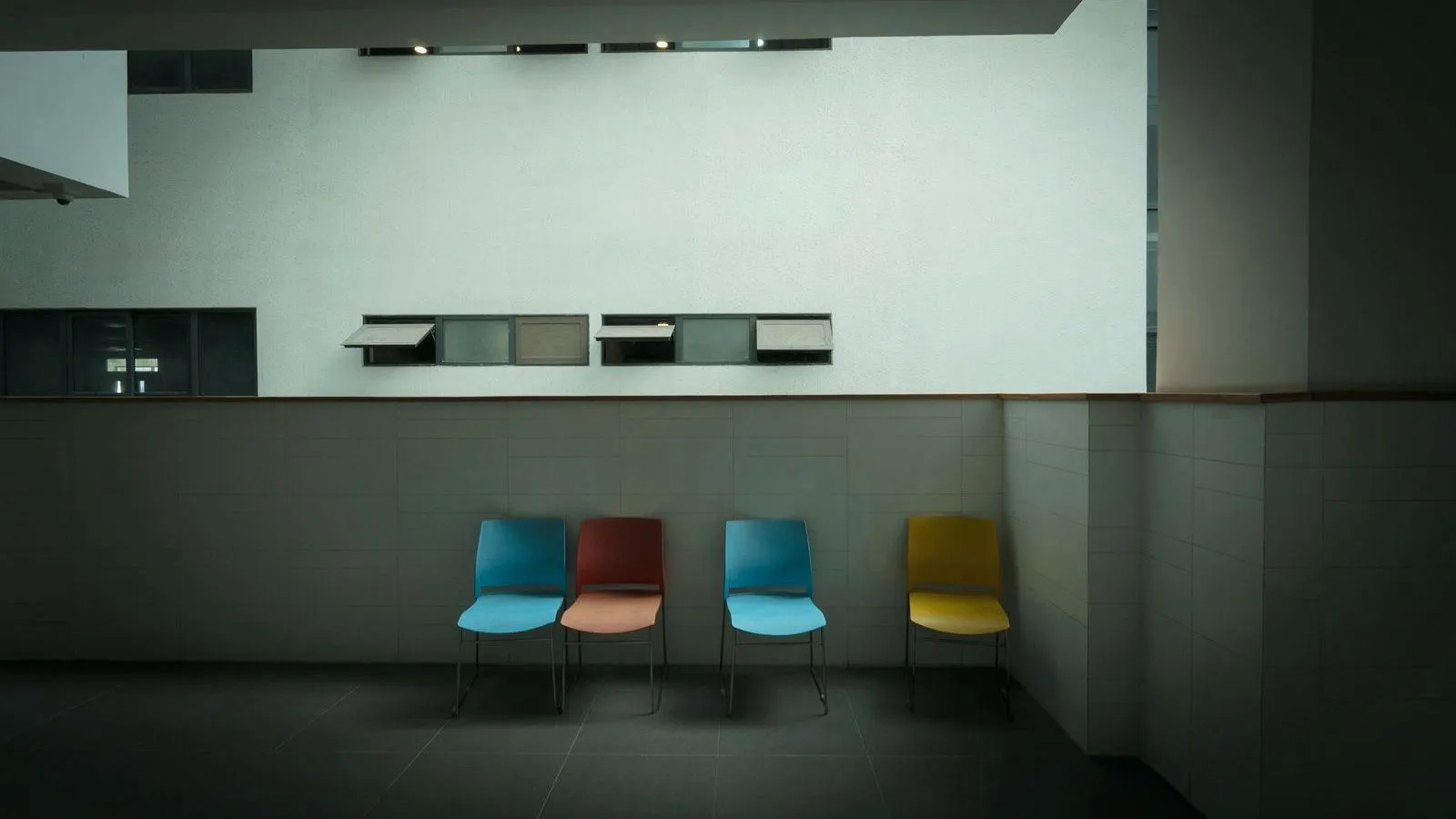 Four empty chairs against a wall in a dimly lit hospital waiting area