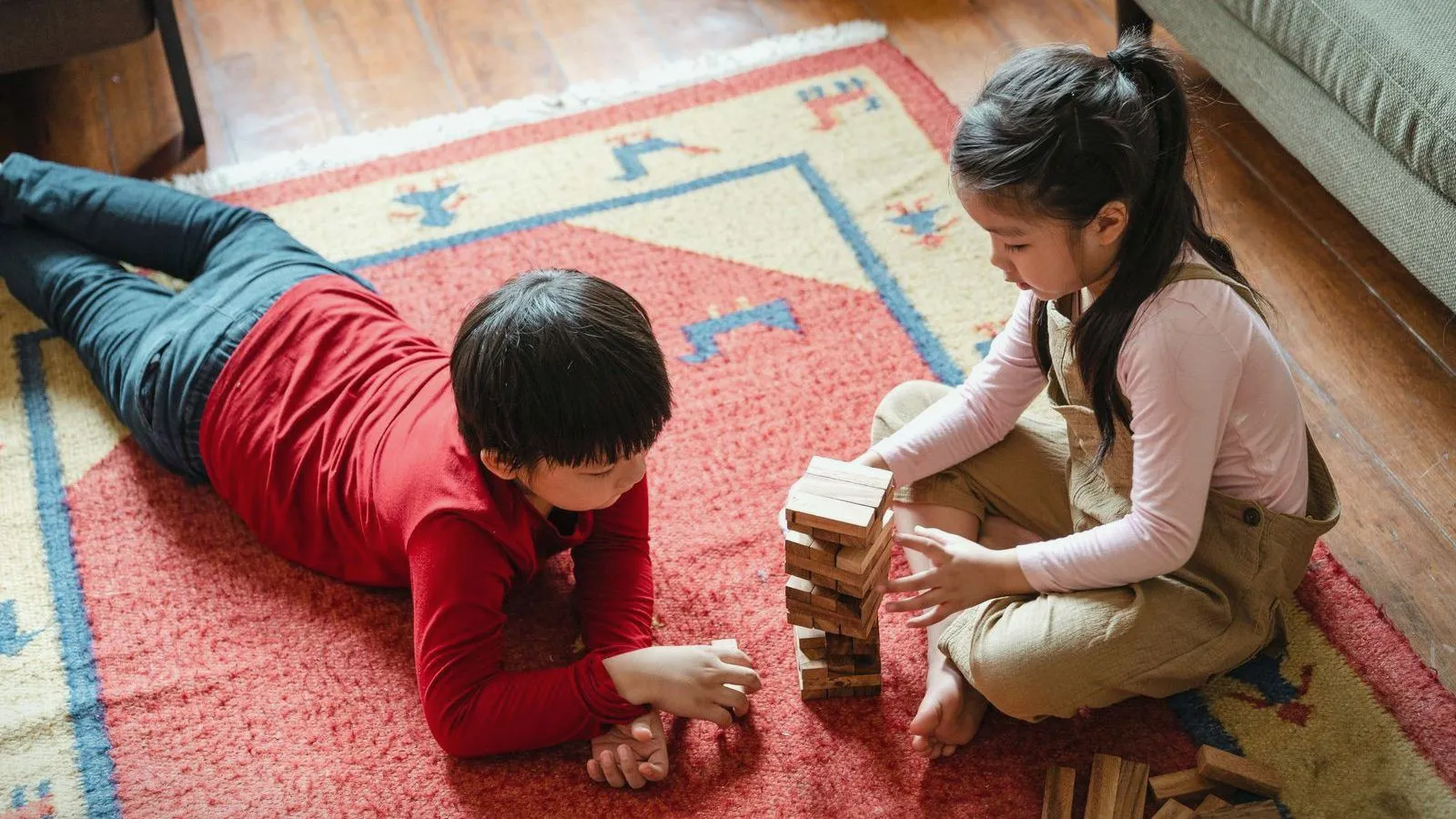 Two children playing with a stack of wooden blocks on a rug