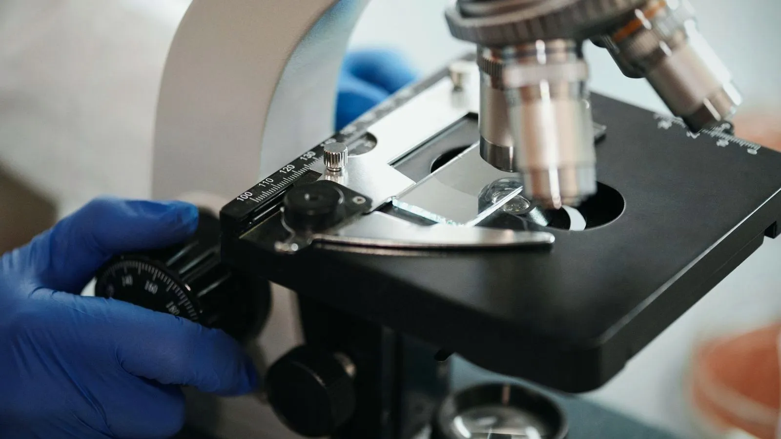 A gloved scientist adjusting a slide on a laboratory microscope