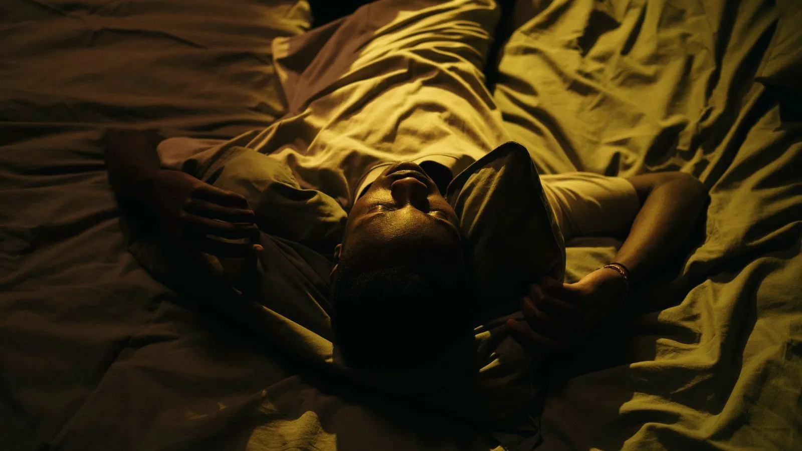 A man lying on his back in bed in a dark room at night