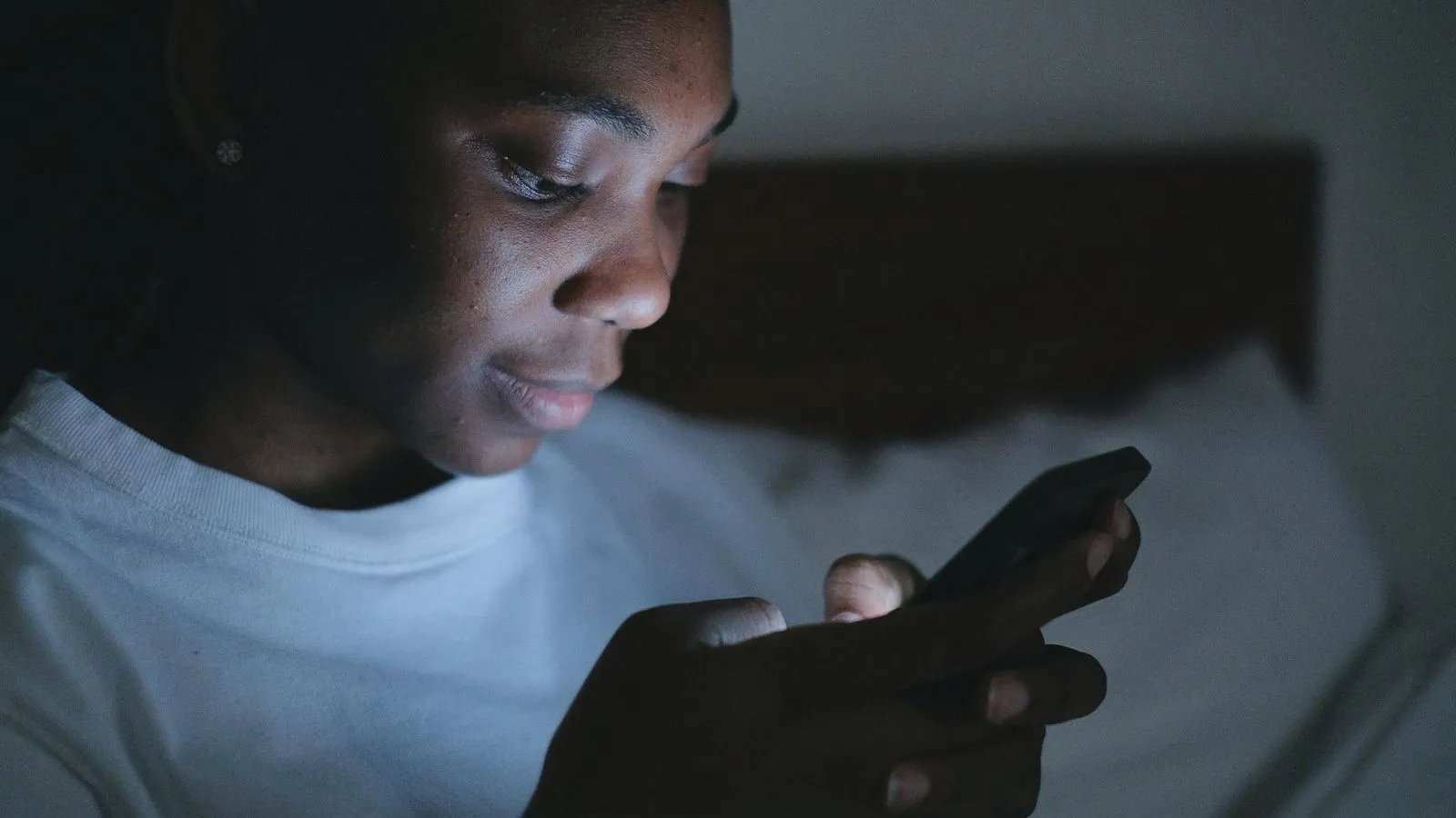 A teenager lit by a phone screen in a dark bedroom