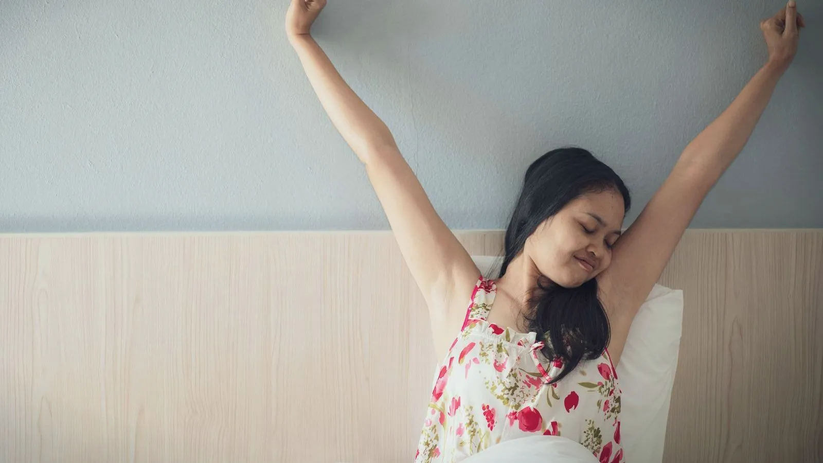 A woman stretching her arms as she wakes up in bed