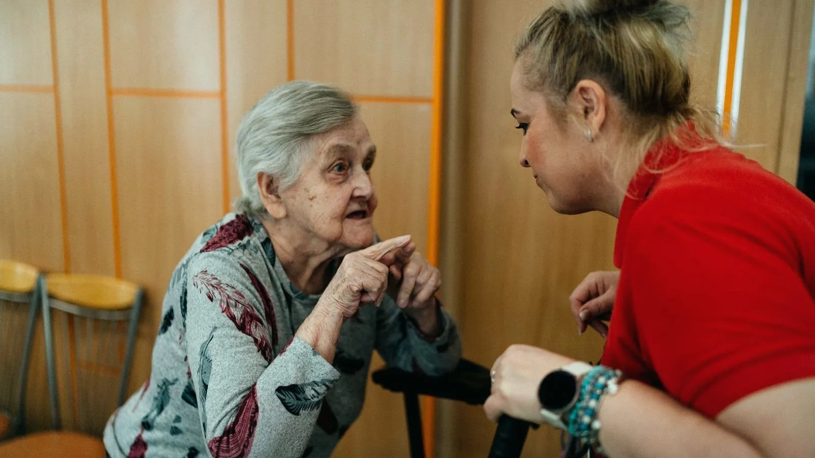An older woman in conversation with a support worker leaning in to listen