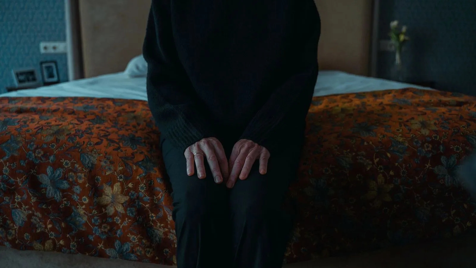 A person sitting on the edge of a bed with hands on their knees