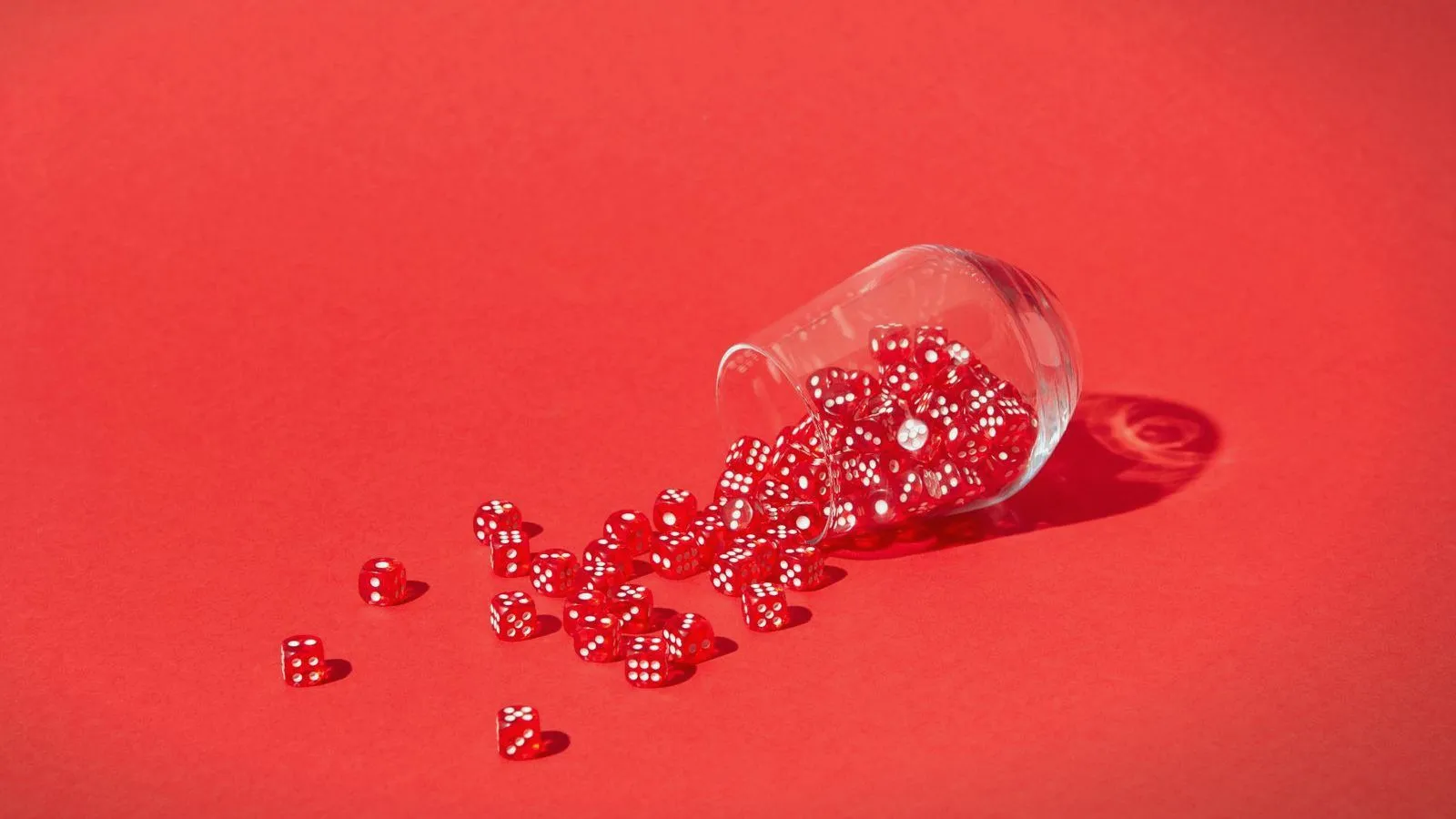 Red sugar-coated sweets spilling from a tipped glass jar on a red background
